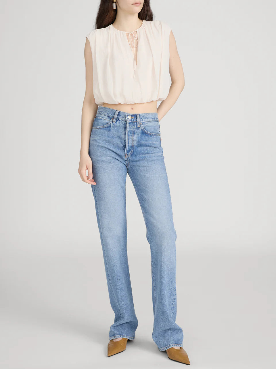 Woman wearing light blue jeans and a beige top on a white background