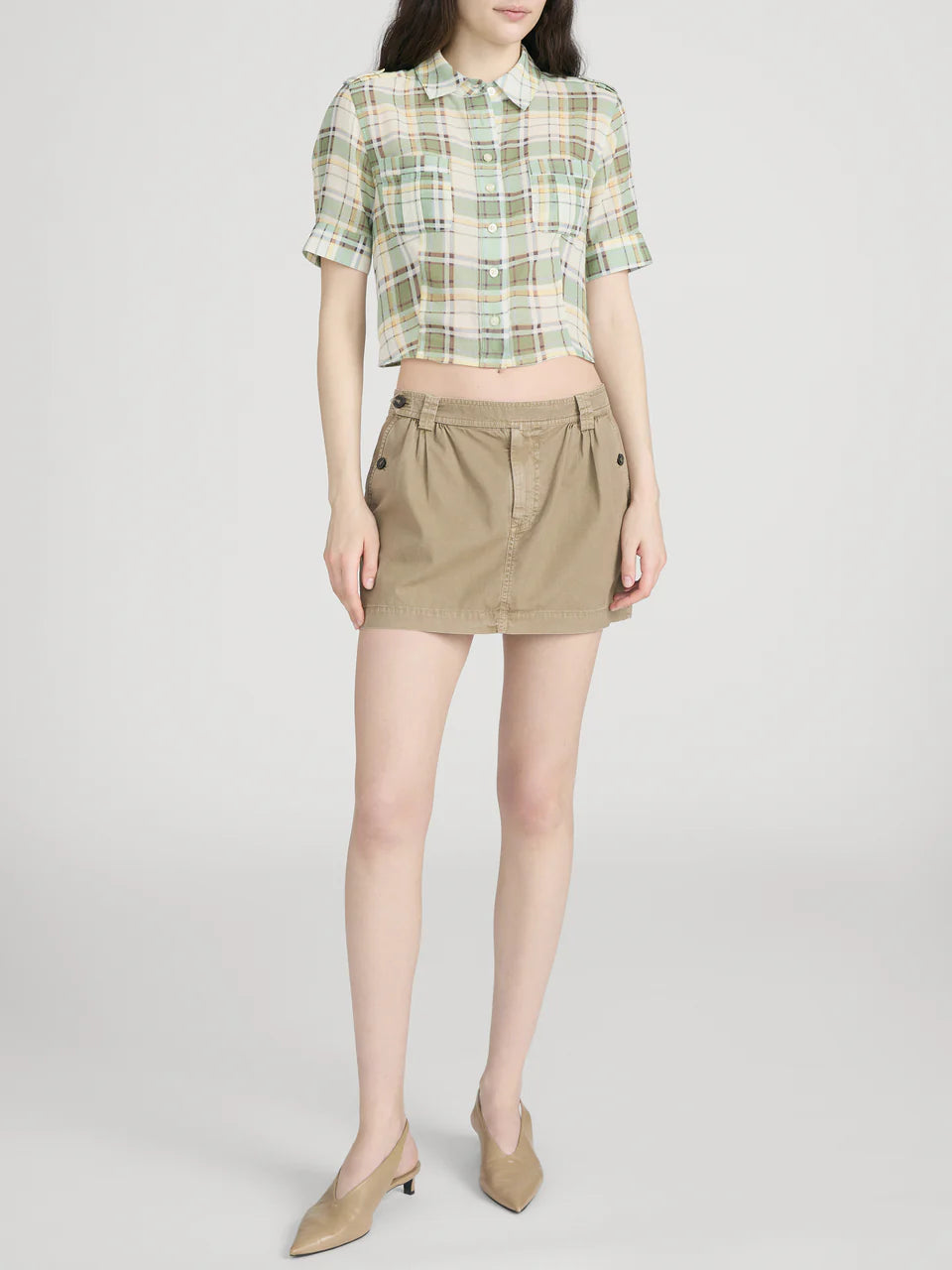 Person wearing a plaid shirt and beige skirt on a white background