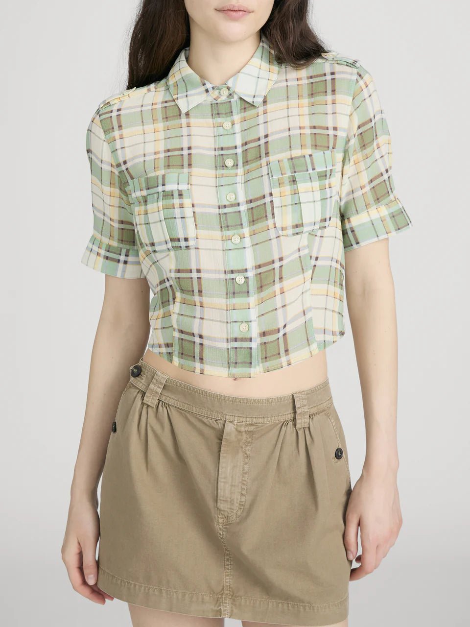 Person wearing a green plaid shirt and beige skirt on a white background