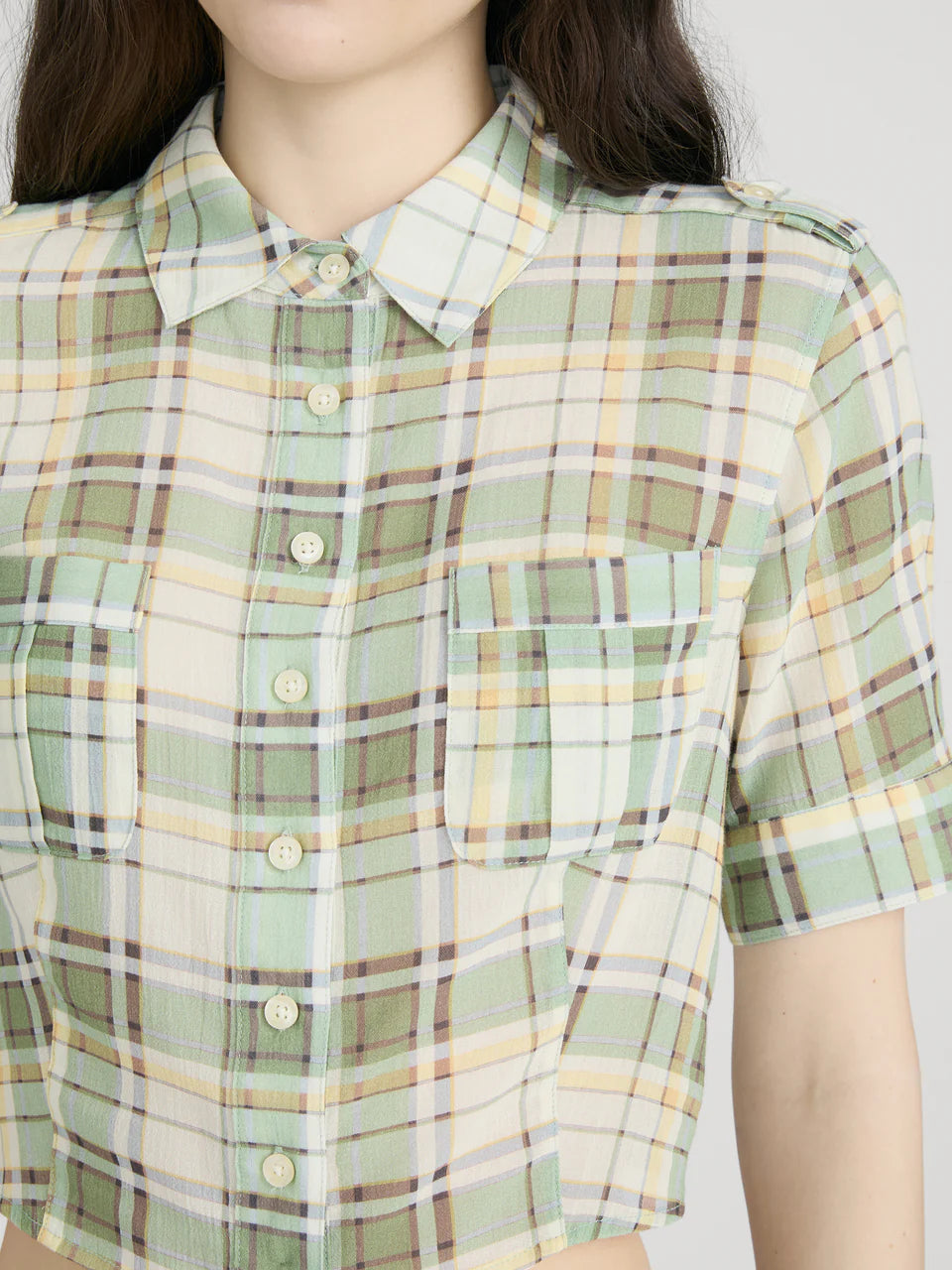 Green and brown plaid shirt worn by a person on a white background