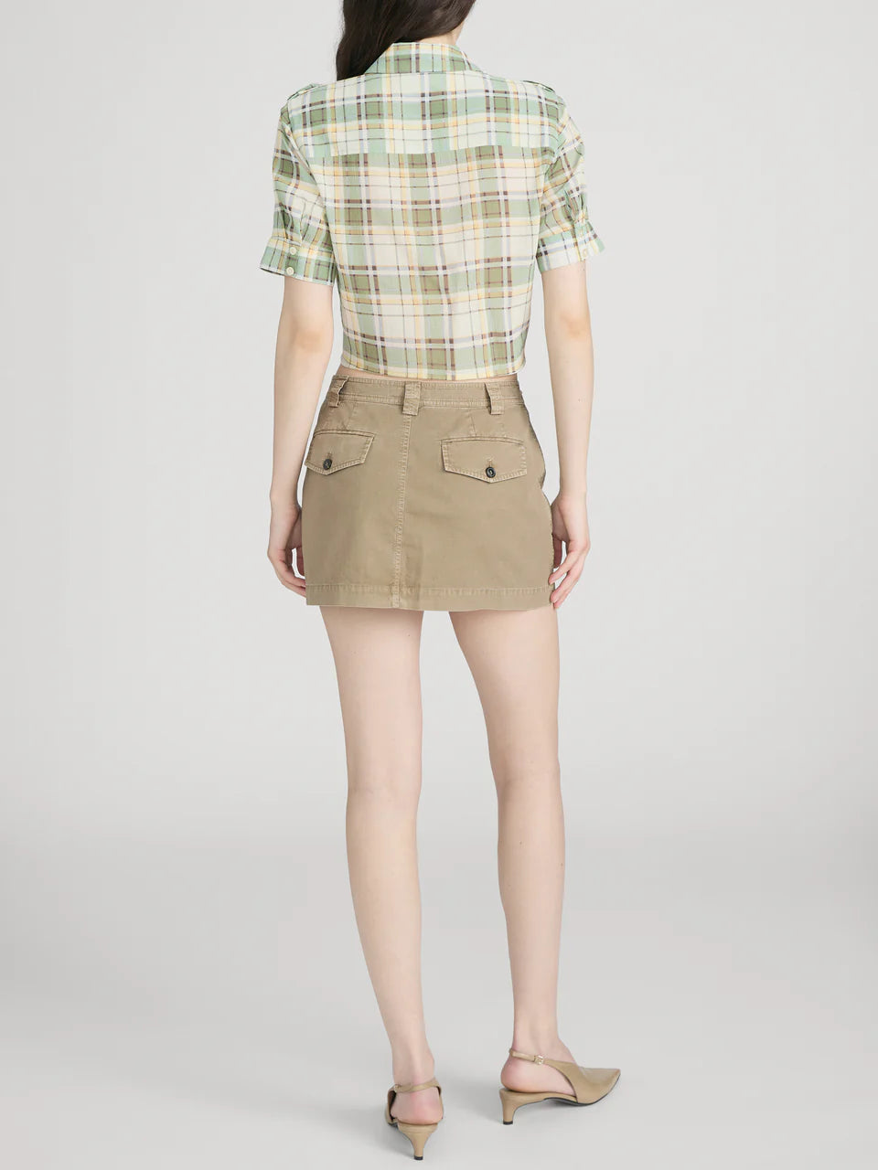 Person wearing a green plaid shirt and beige skirt on a white background