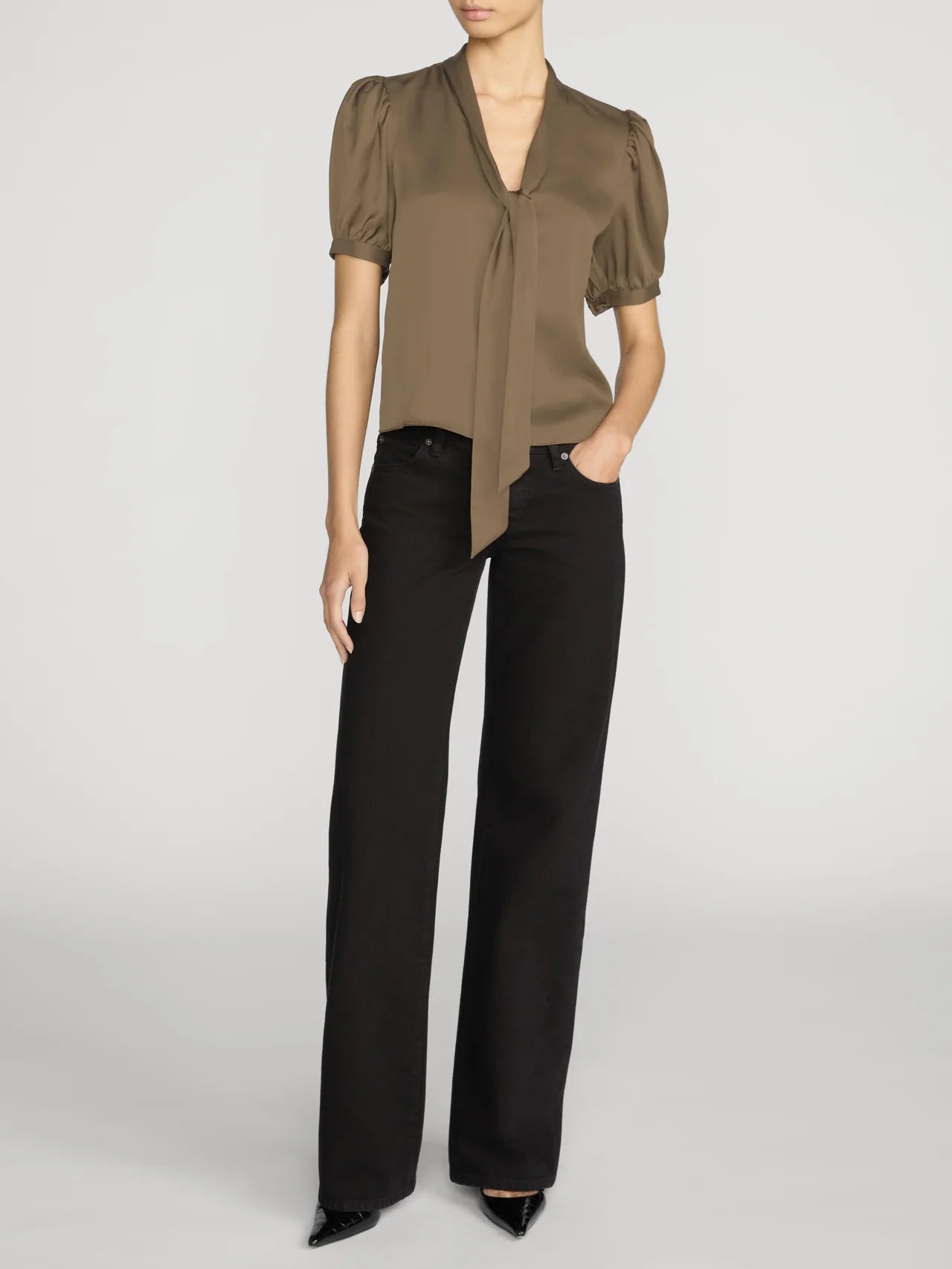 A model wearing a short-sleeved olive-brown satin blouse with puff sleeves and a front tie detail, paired with black wide-leg trousers, against a light gray studio background.