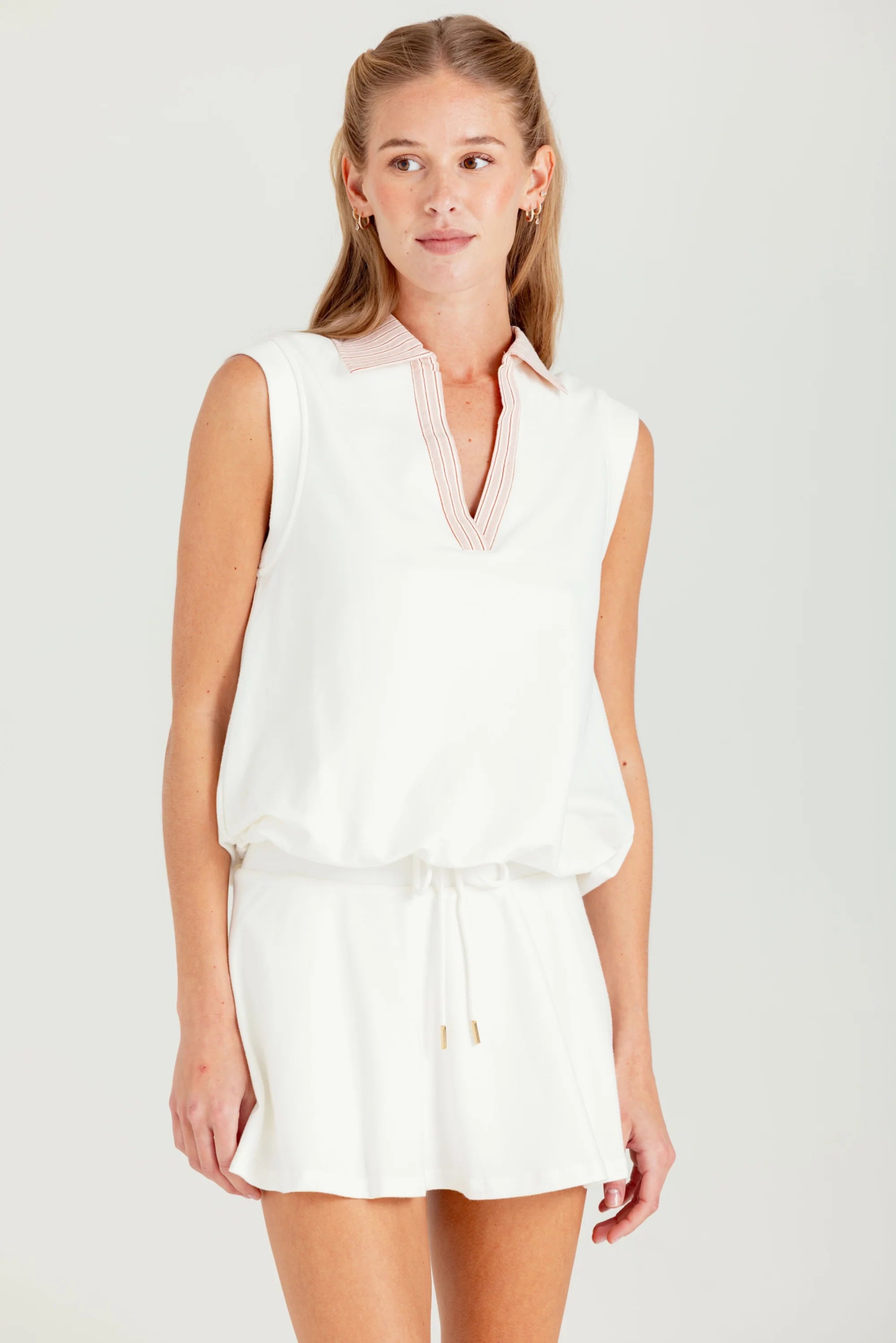 Woman wearing a white sleeveless top and shorts on a plain background