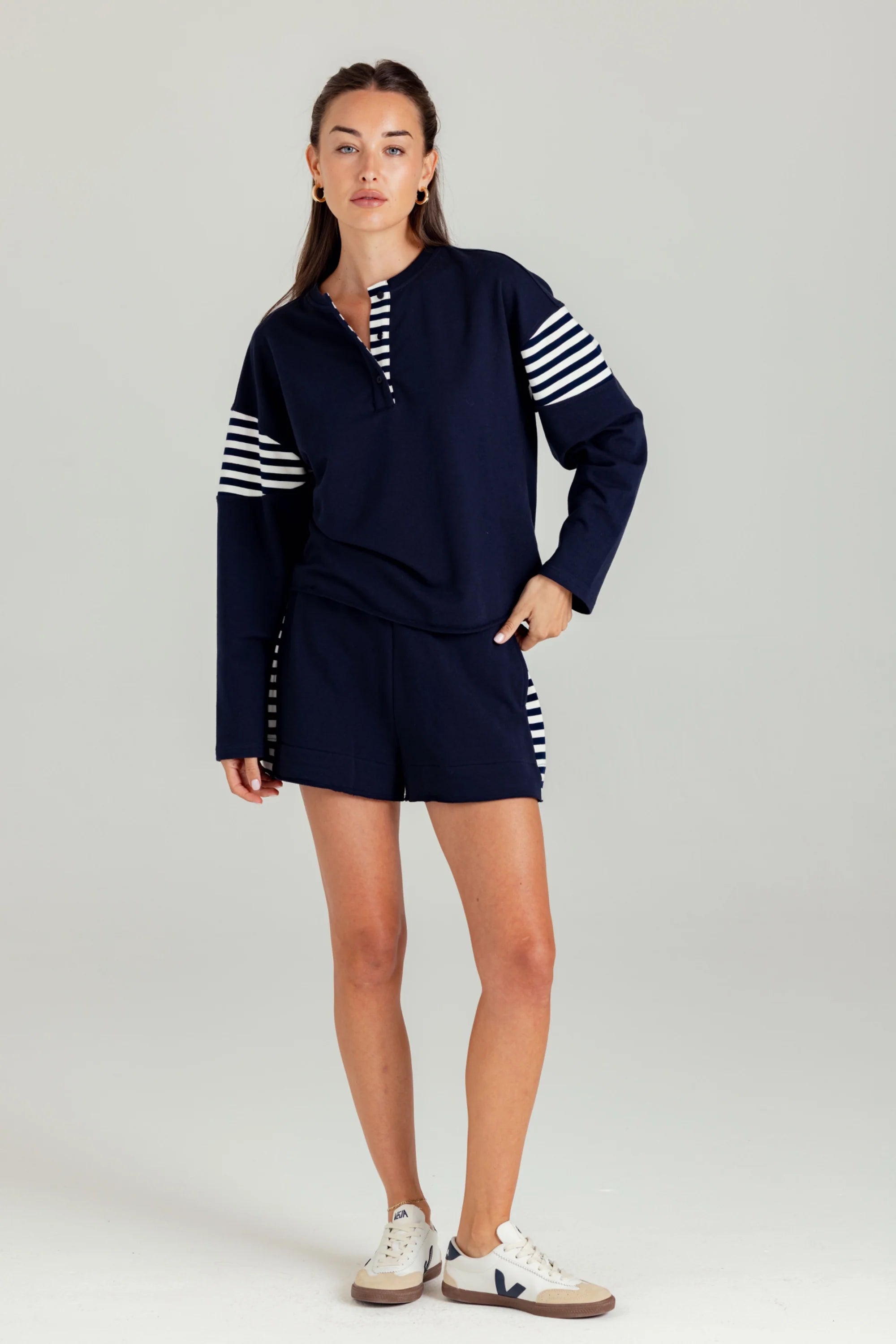 Woman wearing a navy tracksuit with white stripes on a light gray background