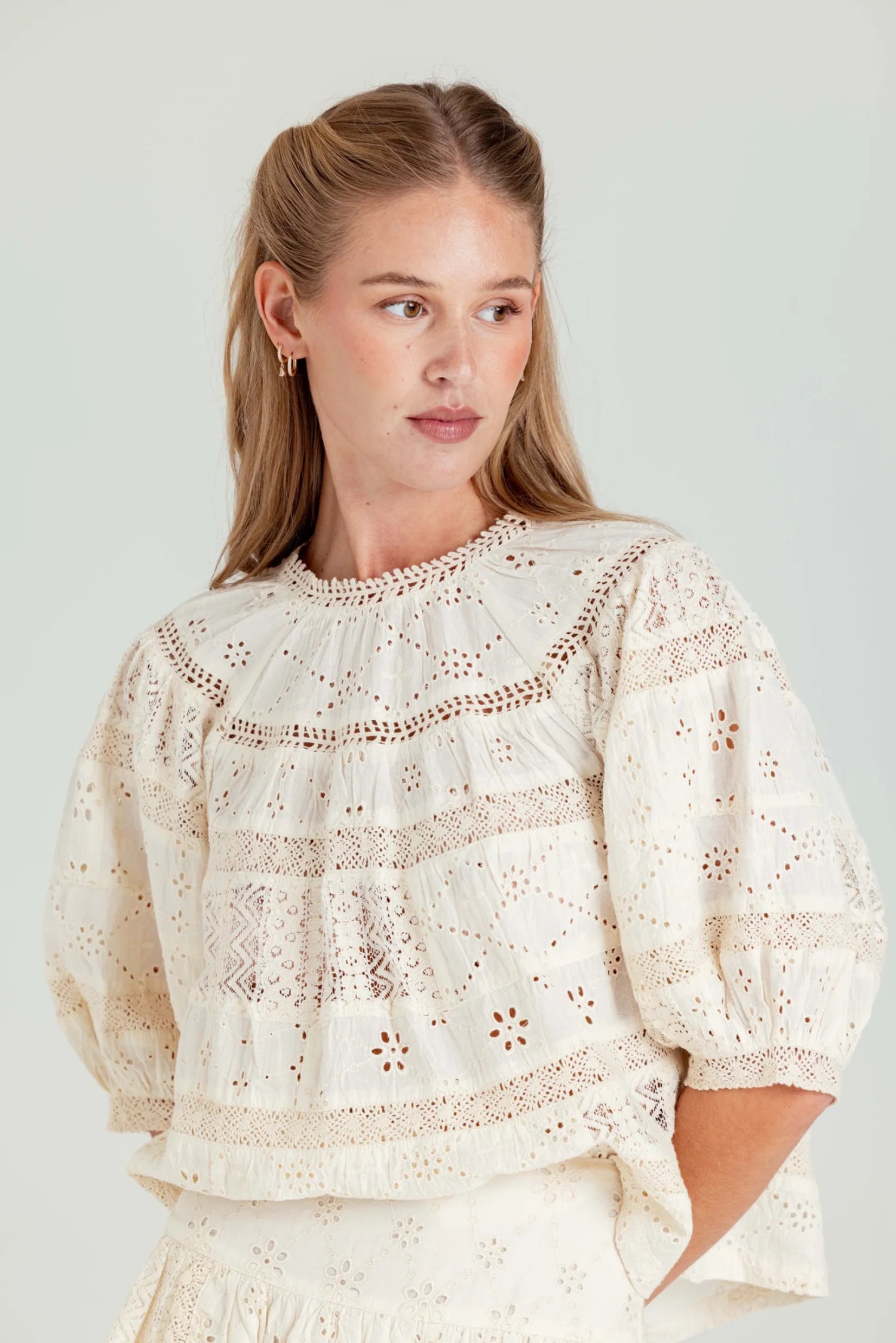 Woman wearing a cream-colored lace blouse against a plain background