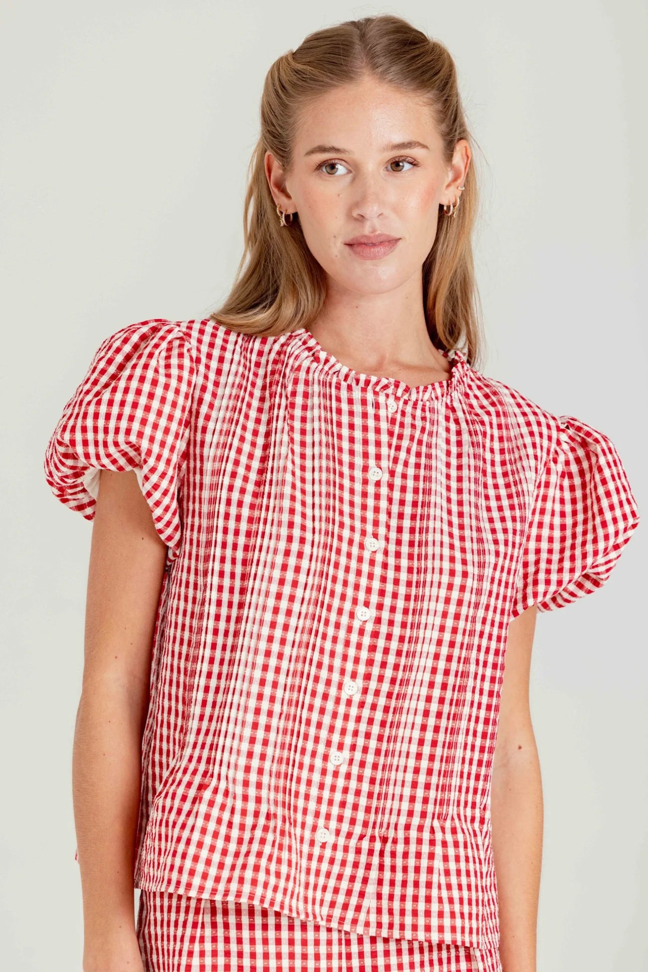 Woman wearing a red and white checkered blouse against a plain background