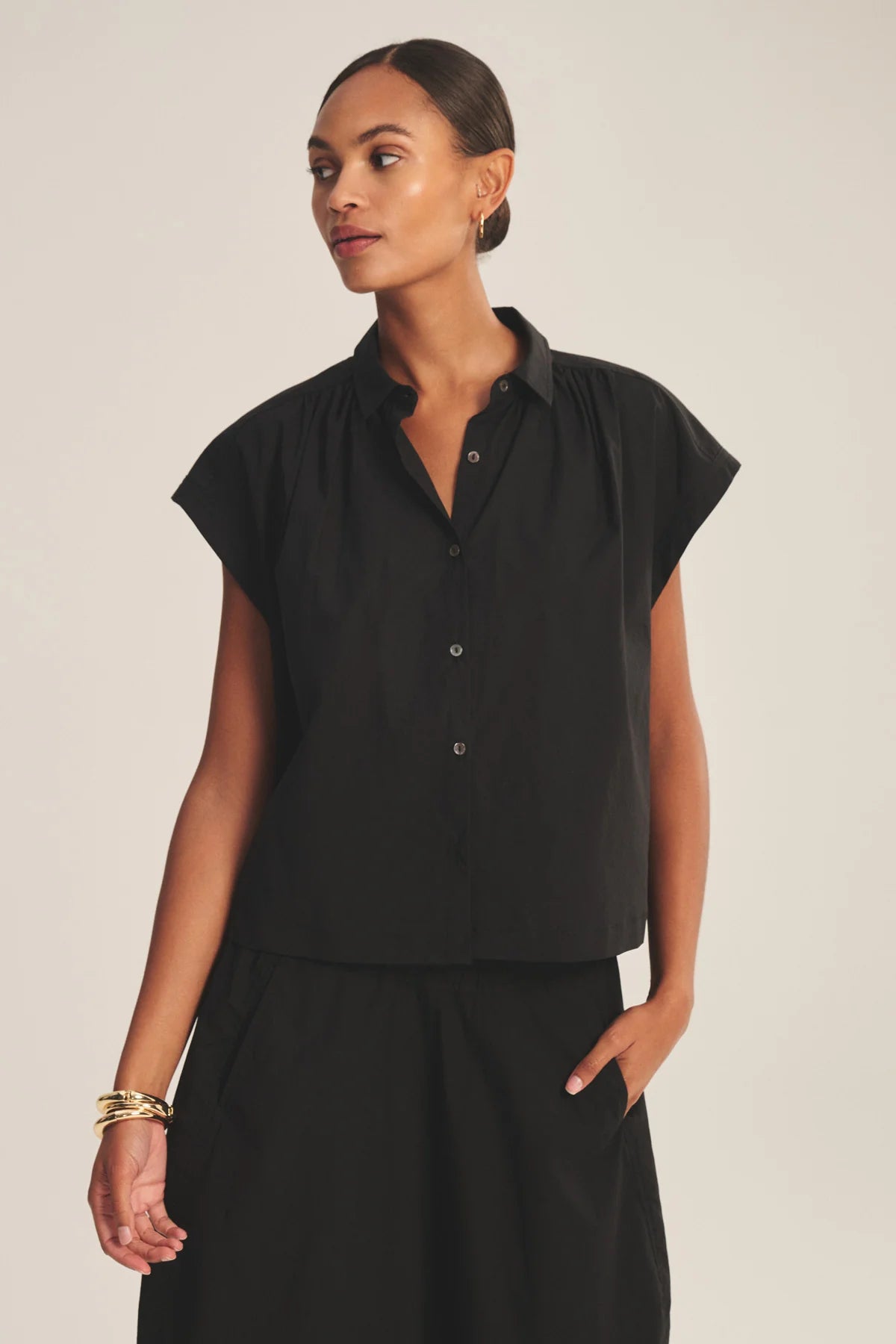 Woman wearing a black sleeveless blouse against a plain background