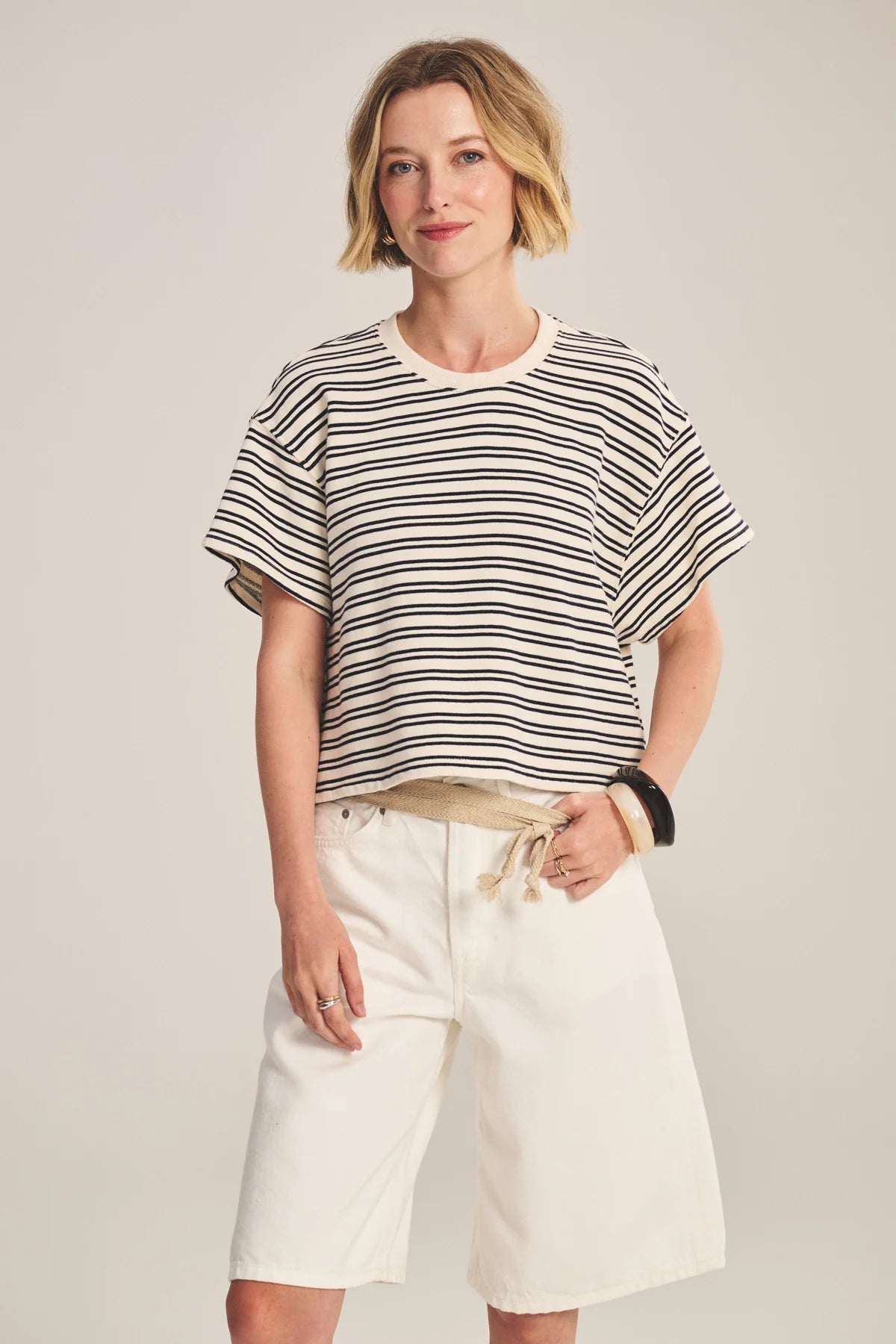Woman wearing a striped shirt and white shorts on a plain background