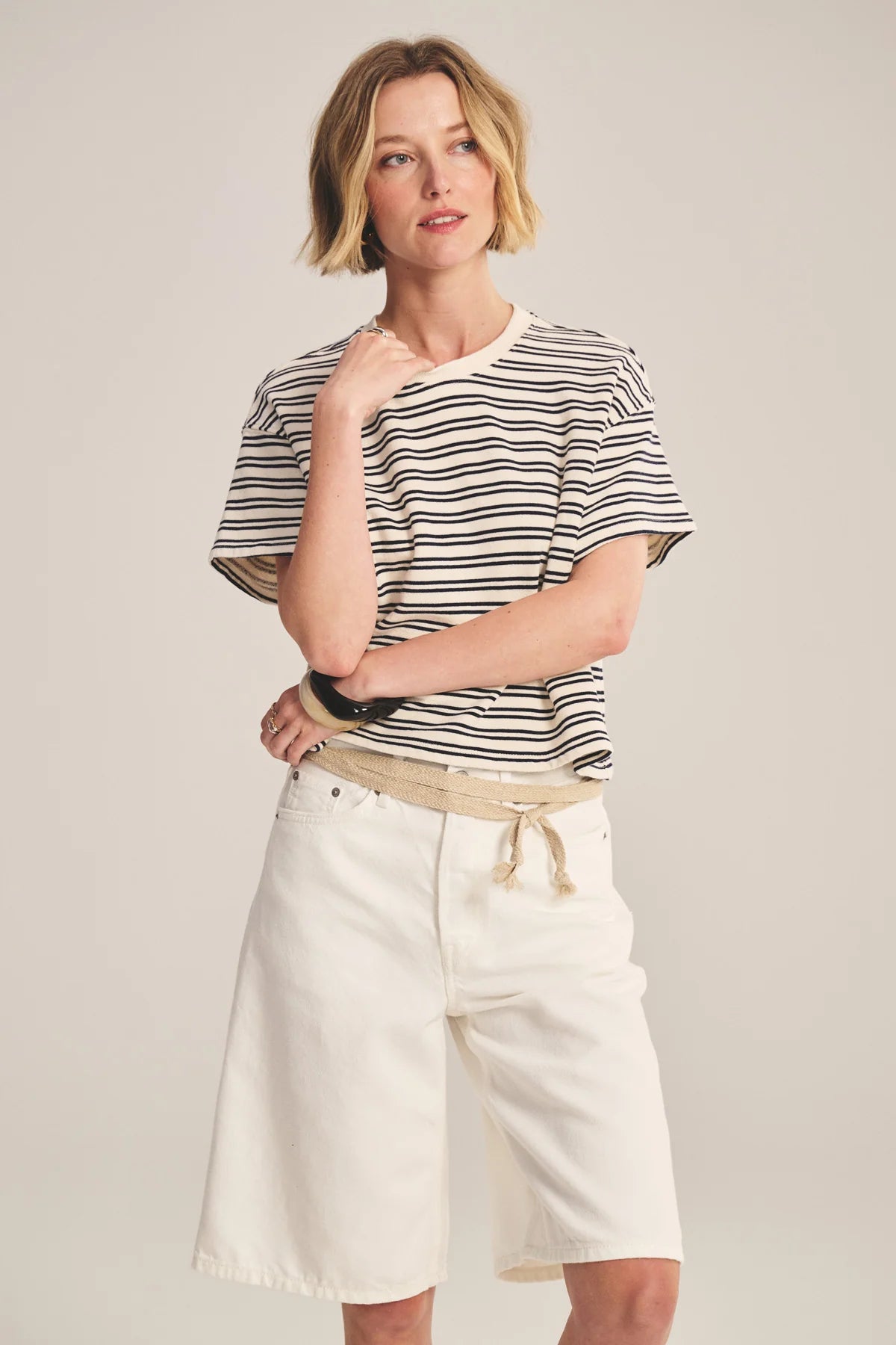 Woman wearing a striped shirt and white shorts on a plain background
