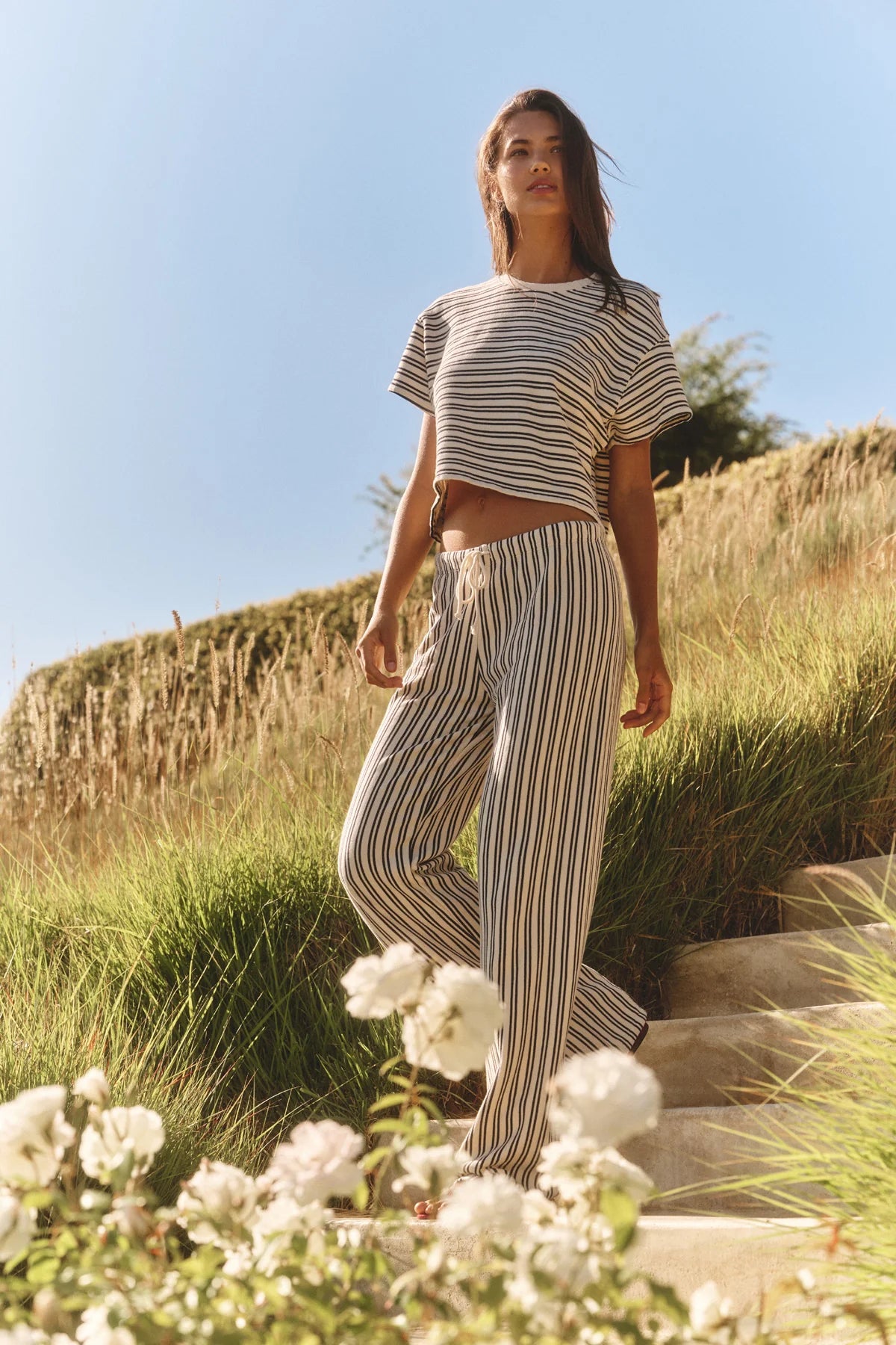 Woman in striped outfit standing on a grassy hill with flowers in the foreground