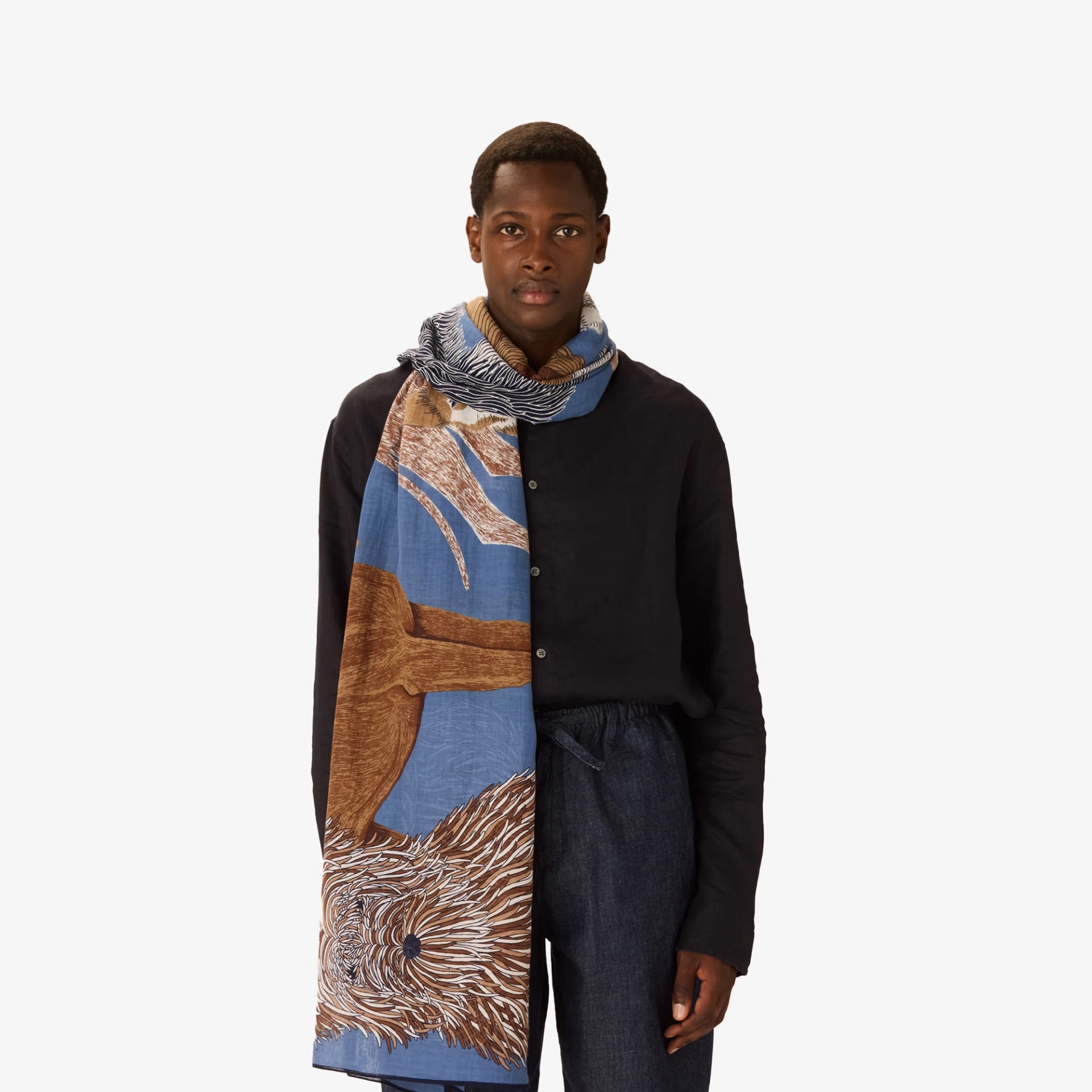 Person wearing a long, patterned scarf with a neutral background