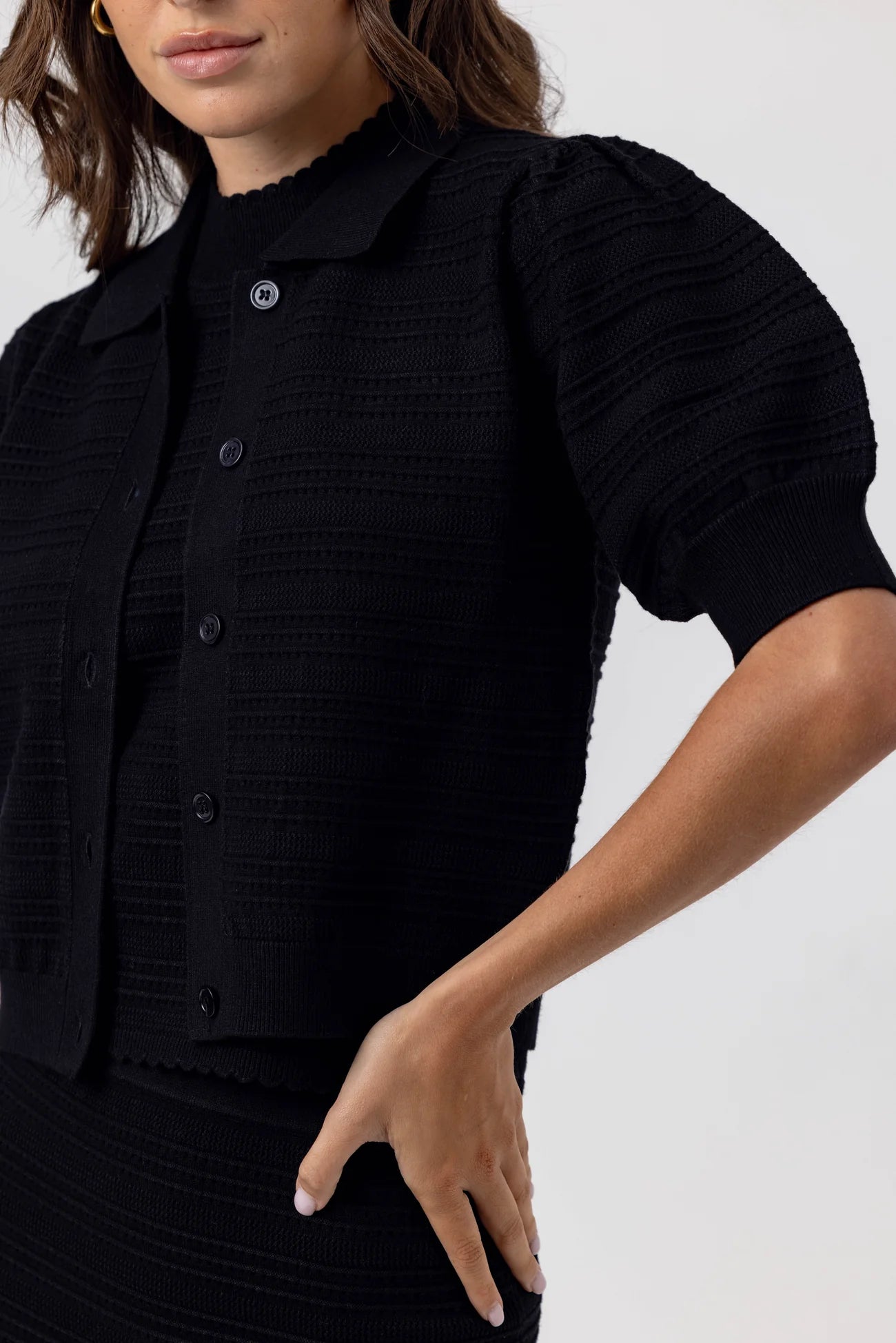 Person wearing a black textured outfit with short sleeves on a white background