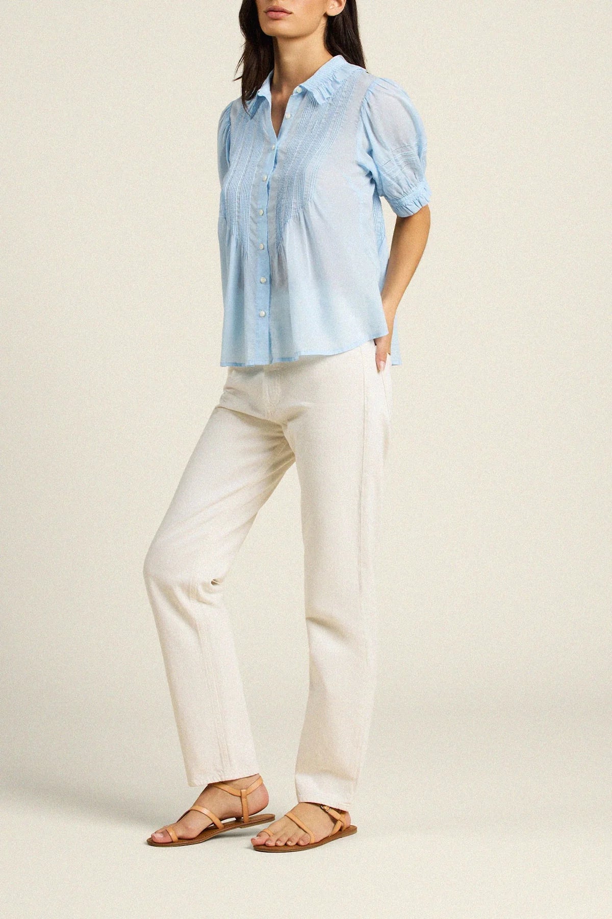 Woman wearing a light blue shirt and white pants on a beige background