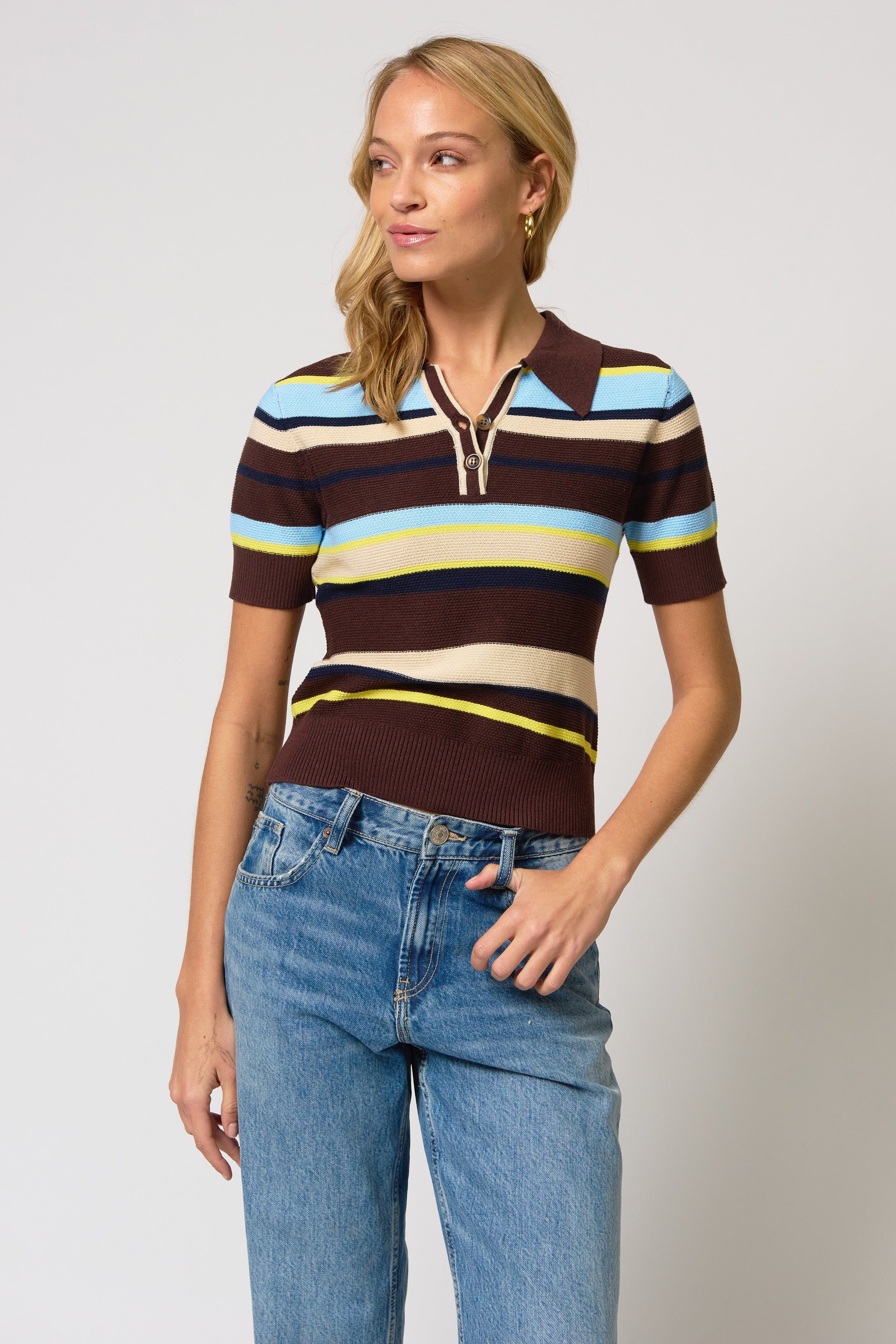 Woman wearing a striped polo shirt and jeans on a plain background