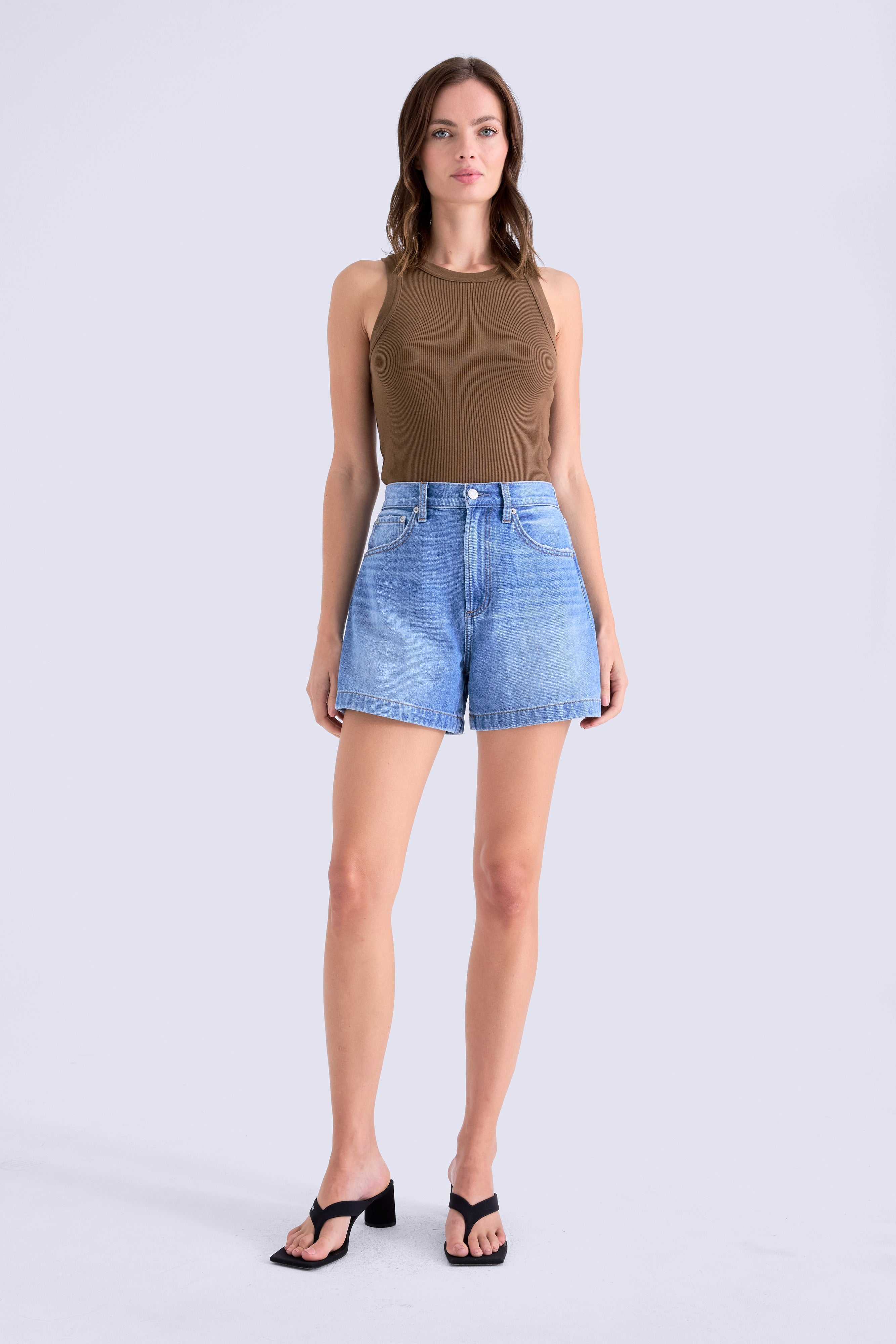Woman wearing a brown sleeveless top and blue denim shorts on a white background