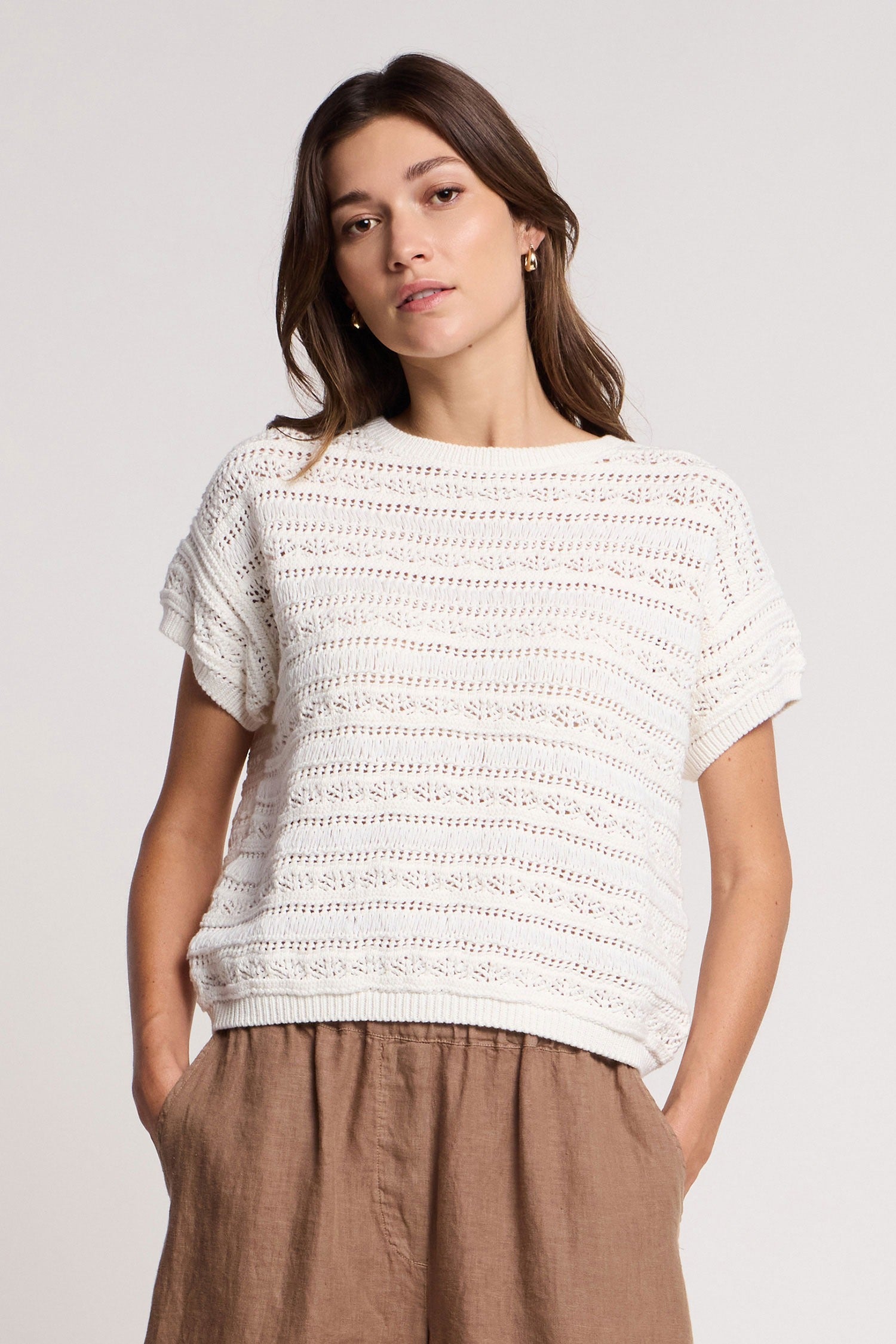Woman wearing a white textured top and brown pants on a plain background