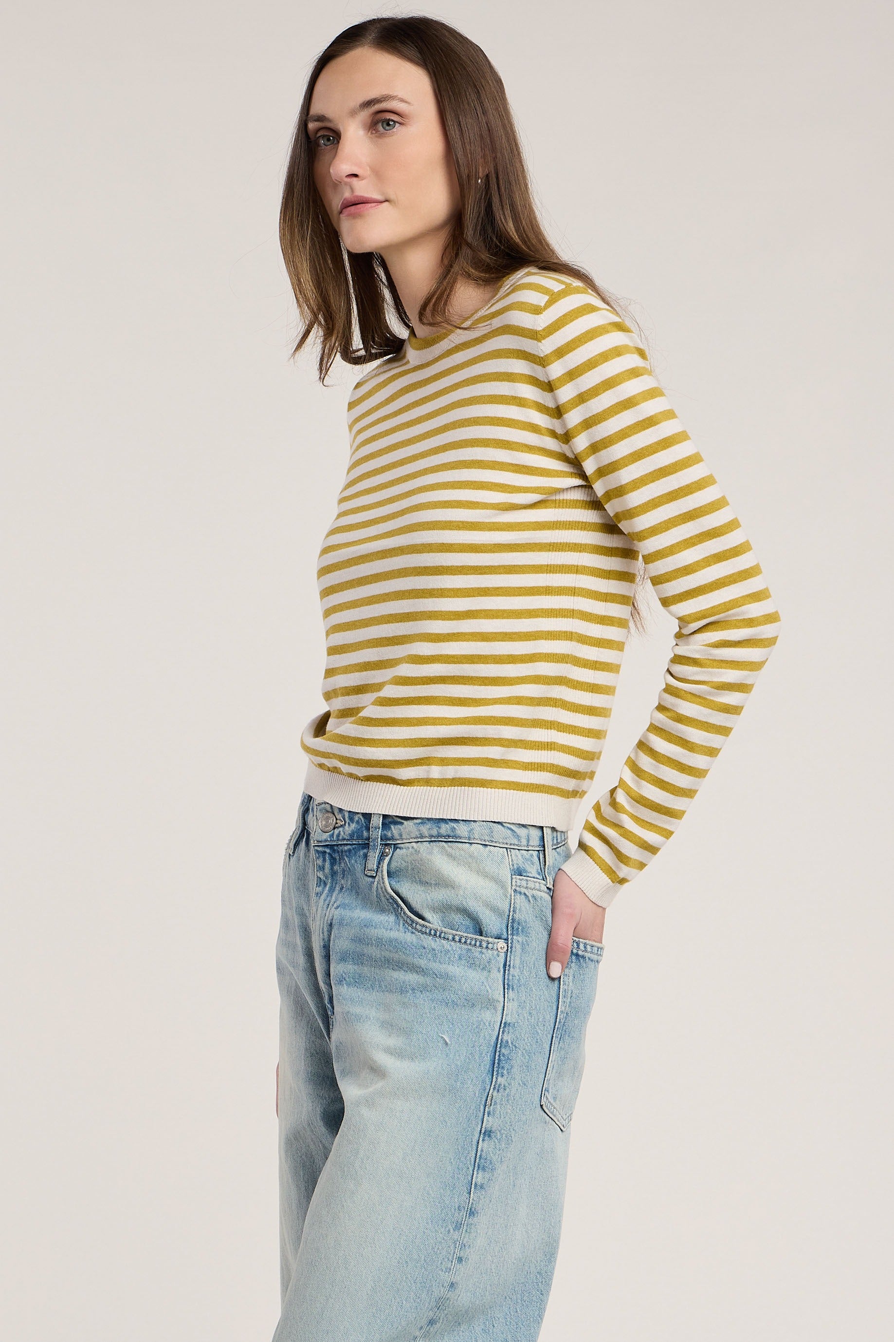 Woman wearing a yellow and white striped sweater and light blue jeans on a plain background