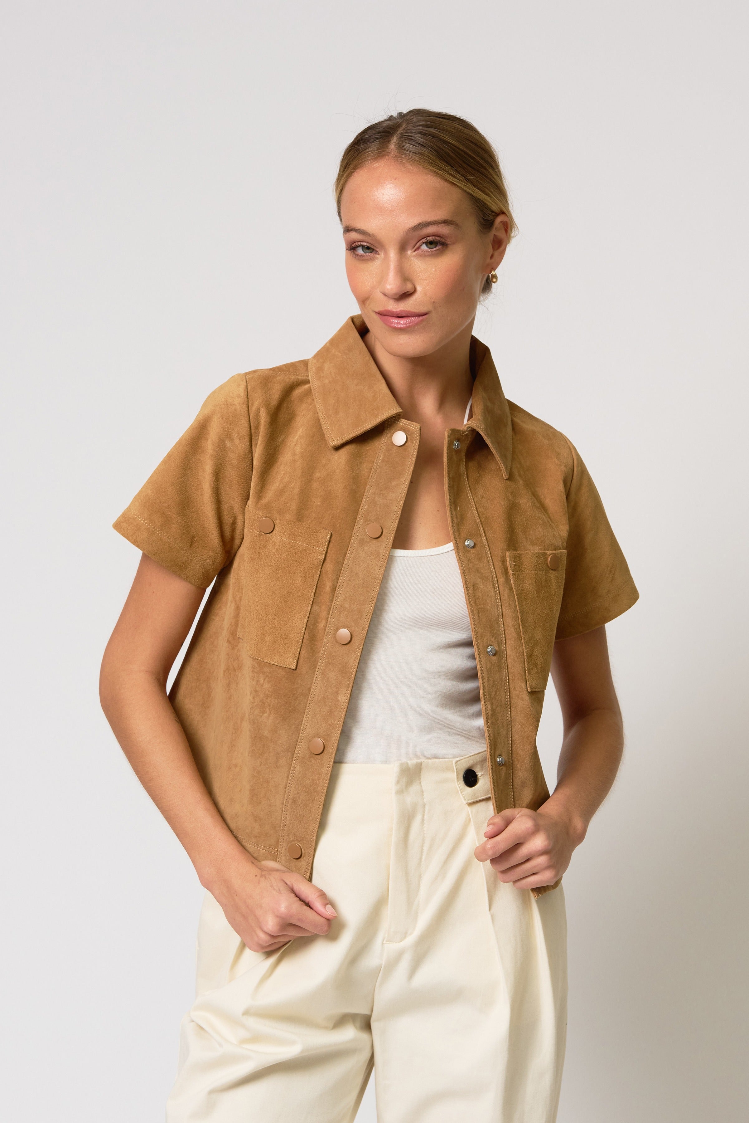 Woman wearing a brown short-sleeve jacket over a white top and beige pants on a light gray background