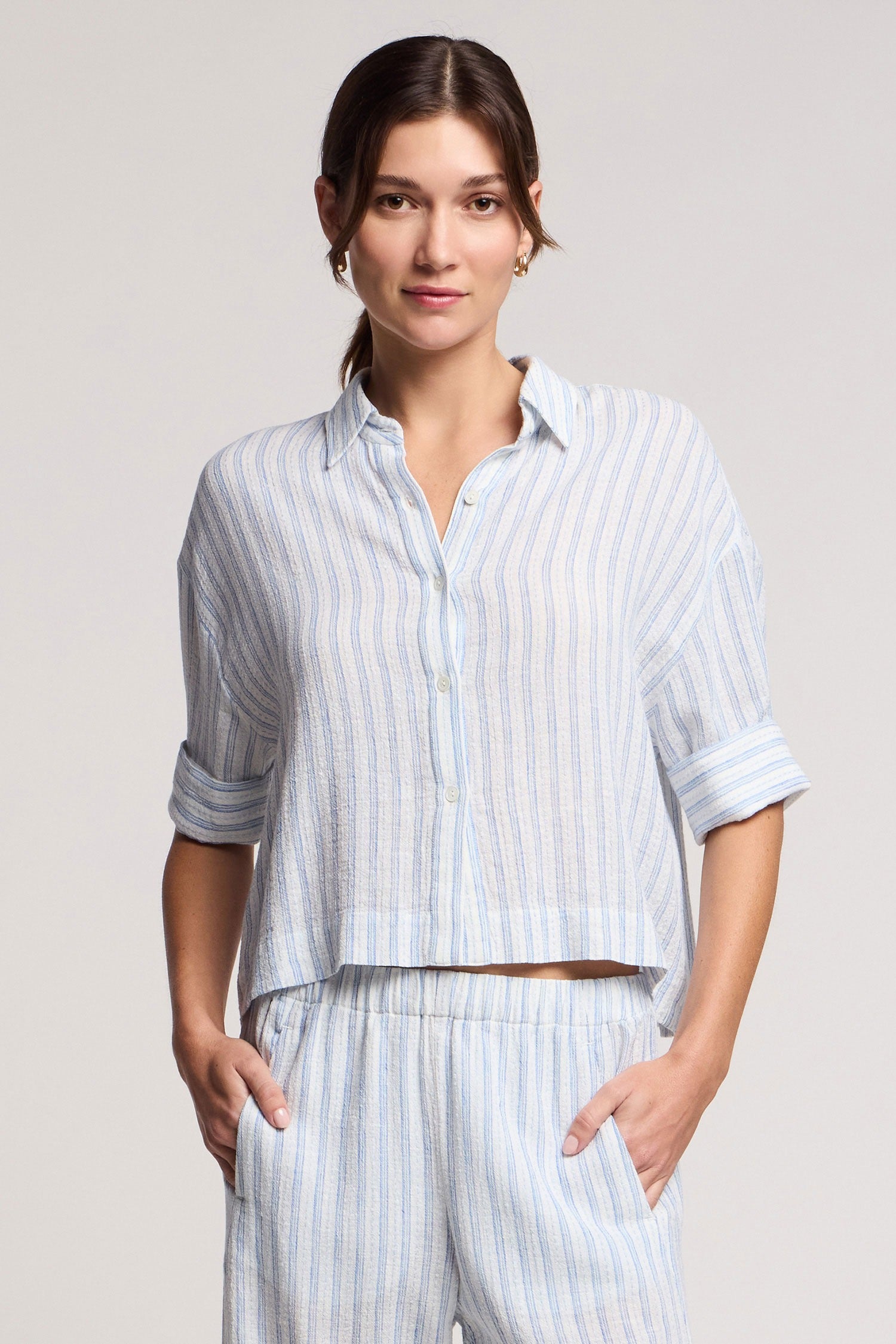 Woman wearing a light blue striped shirt and pants on a plain background