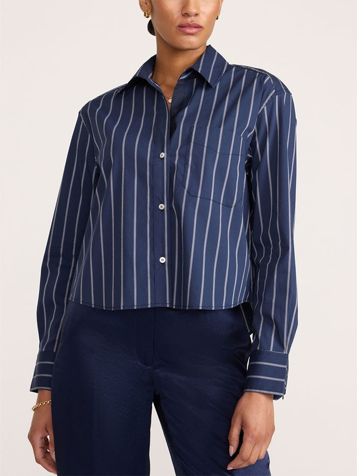 A model wearing a navy blue and white vertically striped cropped button-down shirt with dark navy pants, shown from the neck down against a plain light background.
