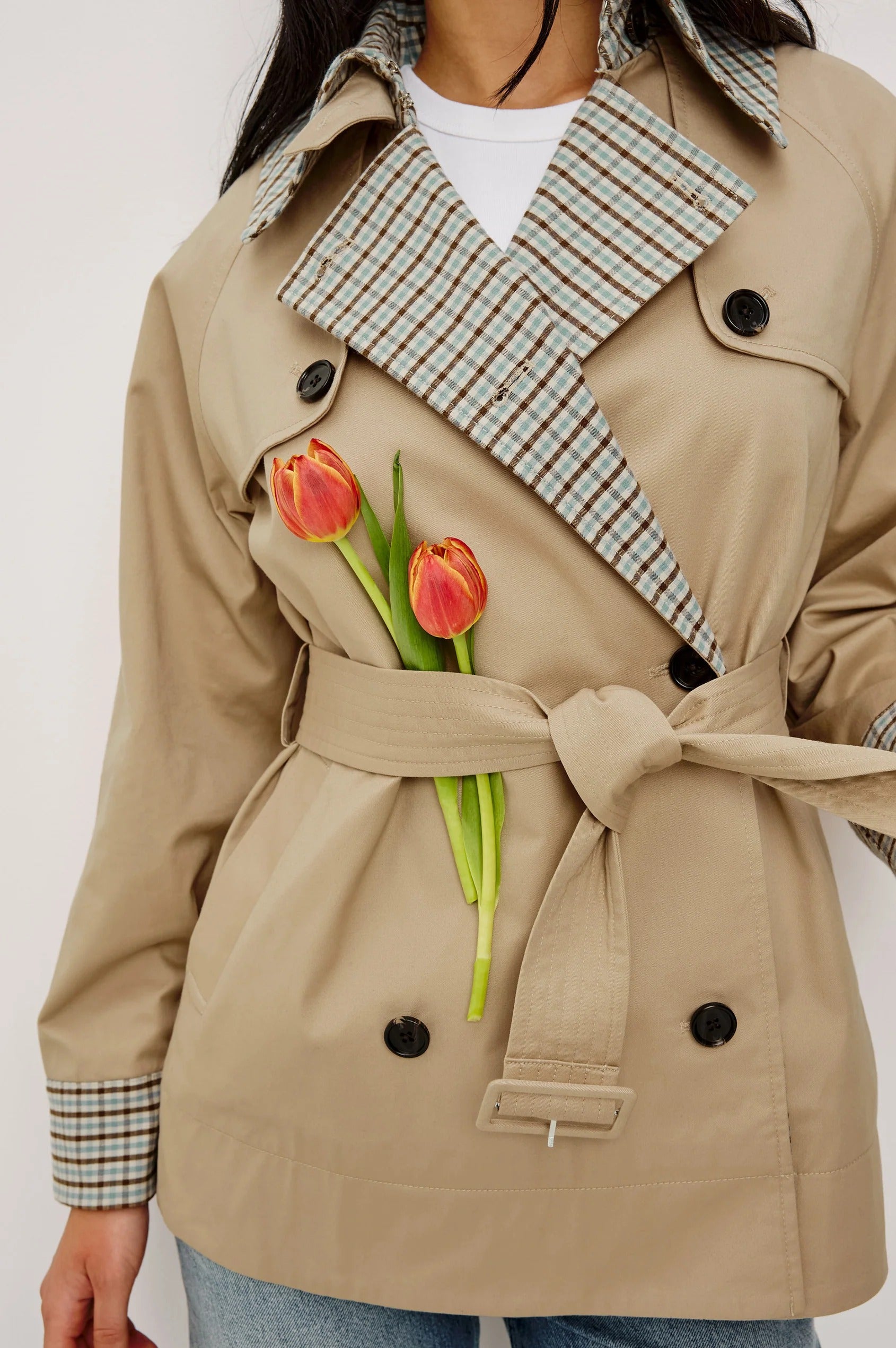 Person wearing a beige trench coat with plaid accents holding tulips.