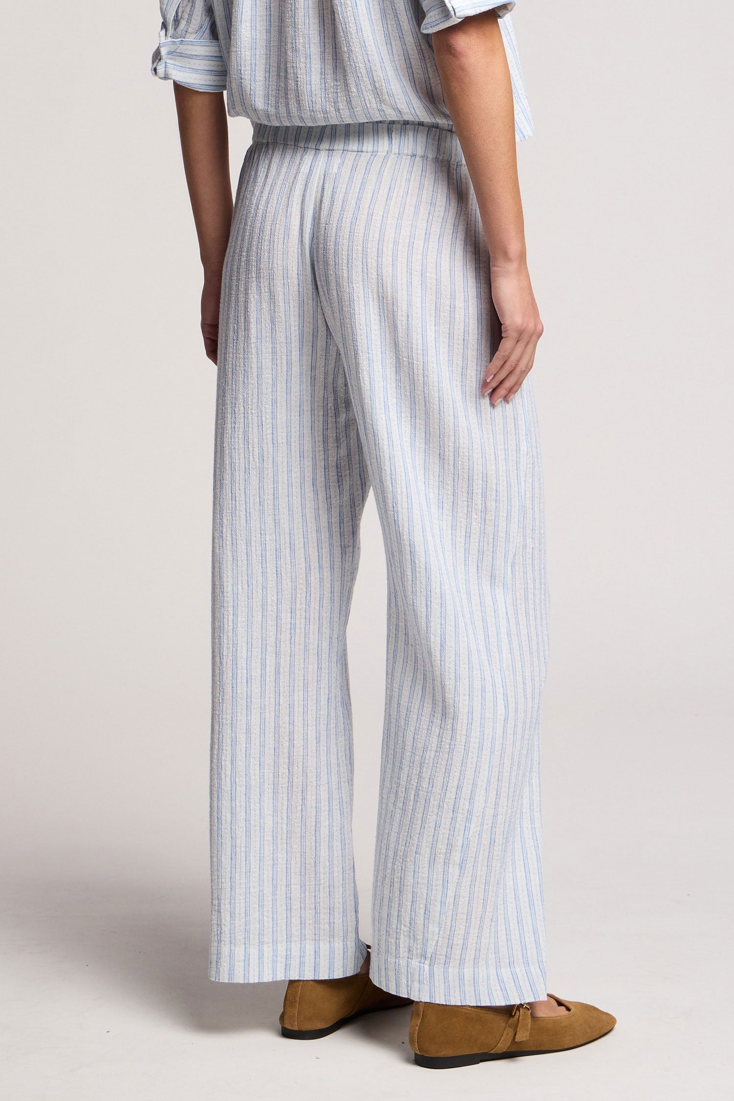 Person wearing a striped outfit with wide-leg pants on a plain background