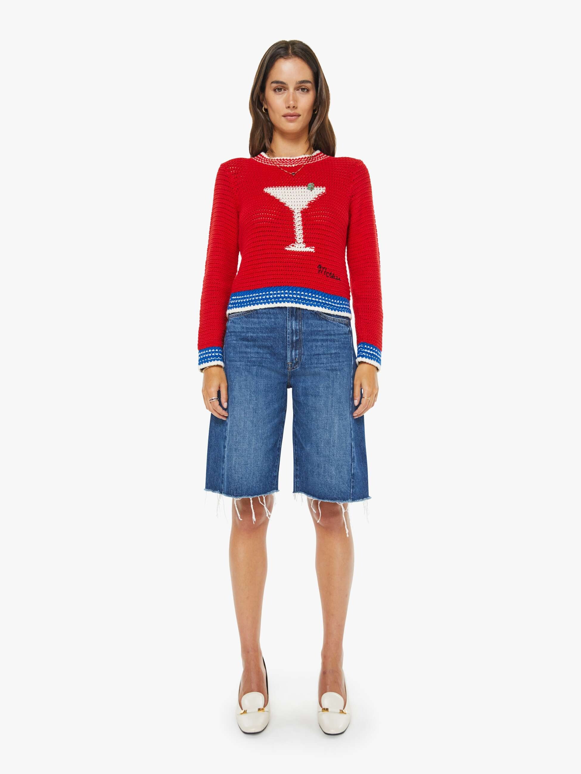 Woman wearing a red sweater with a martini glass design and blue denim shorts on a white background