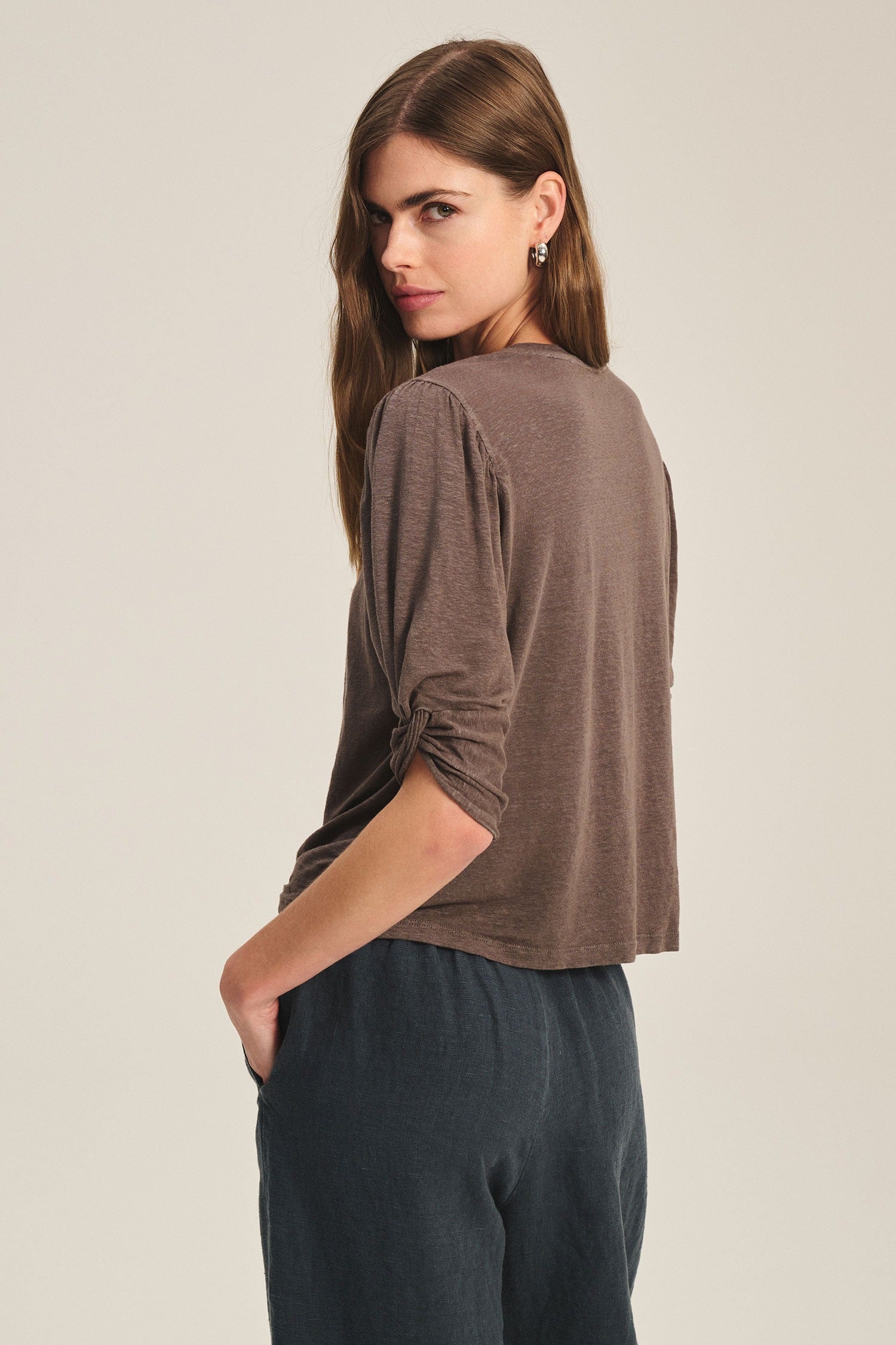 Woman wearing a brown sweater and dark pants against a beige background