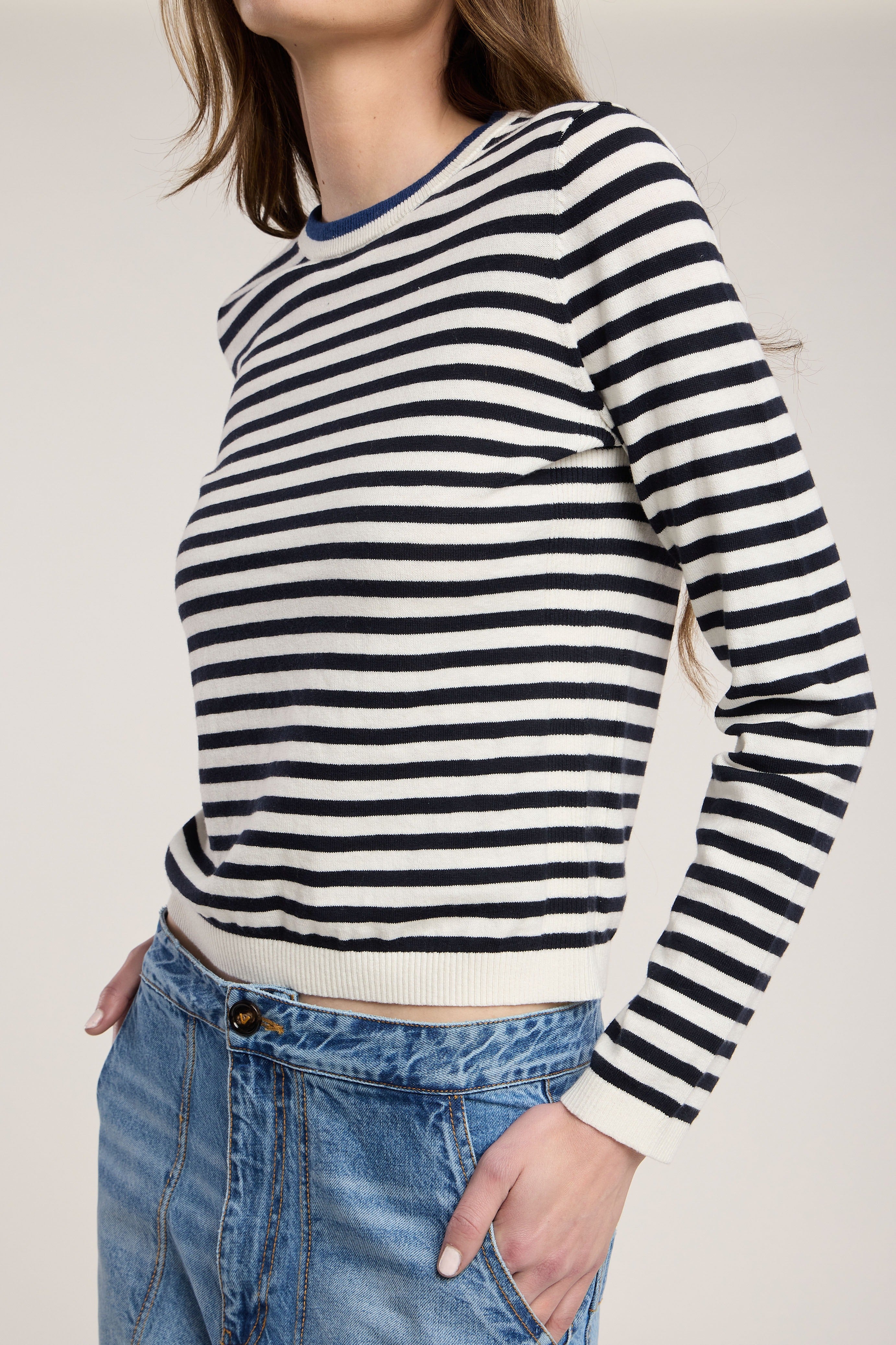 Person wearing a black and white striped sweater with blue jeans on a plain background