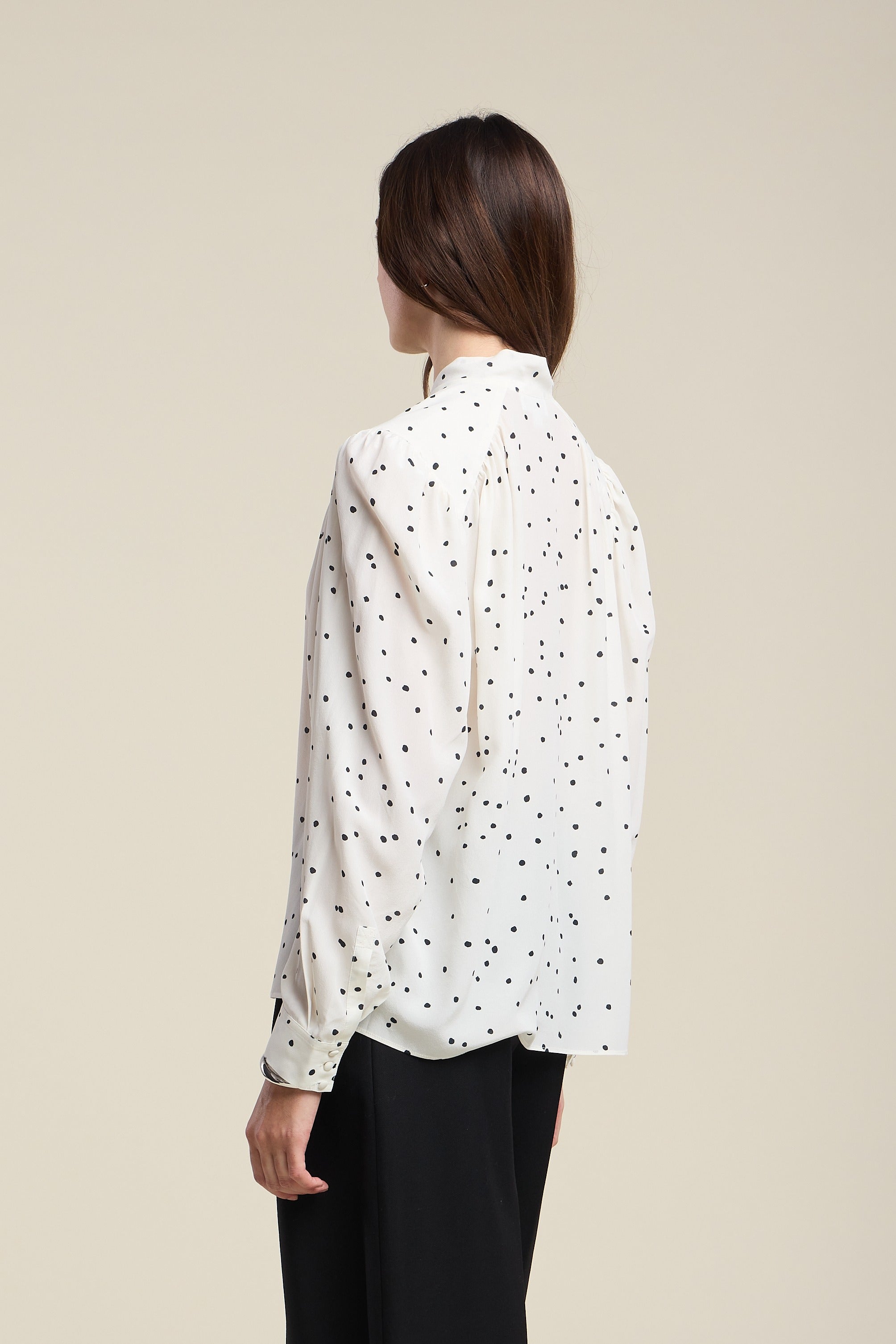 Woman wearing a white blouse with black polka dots on a beige background