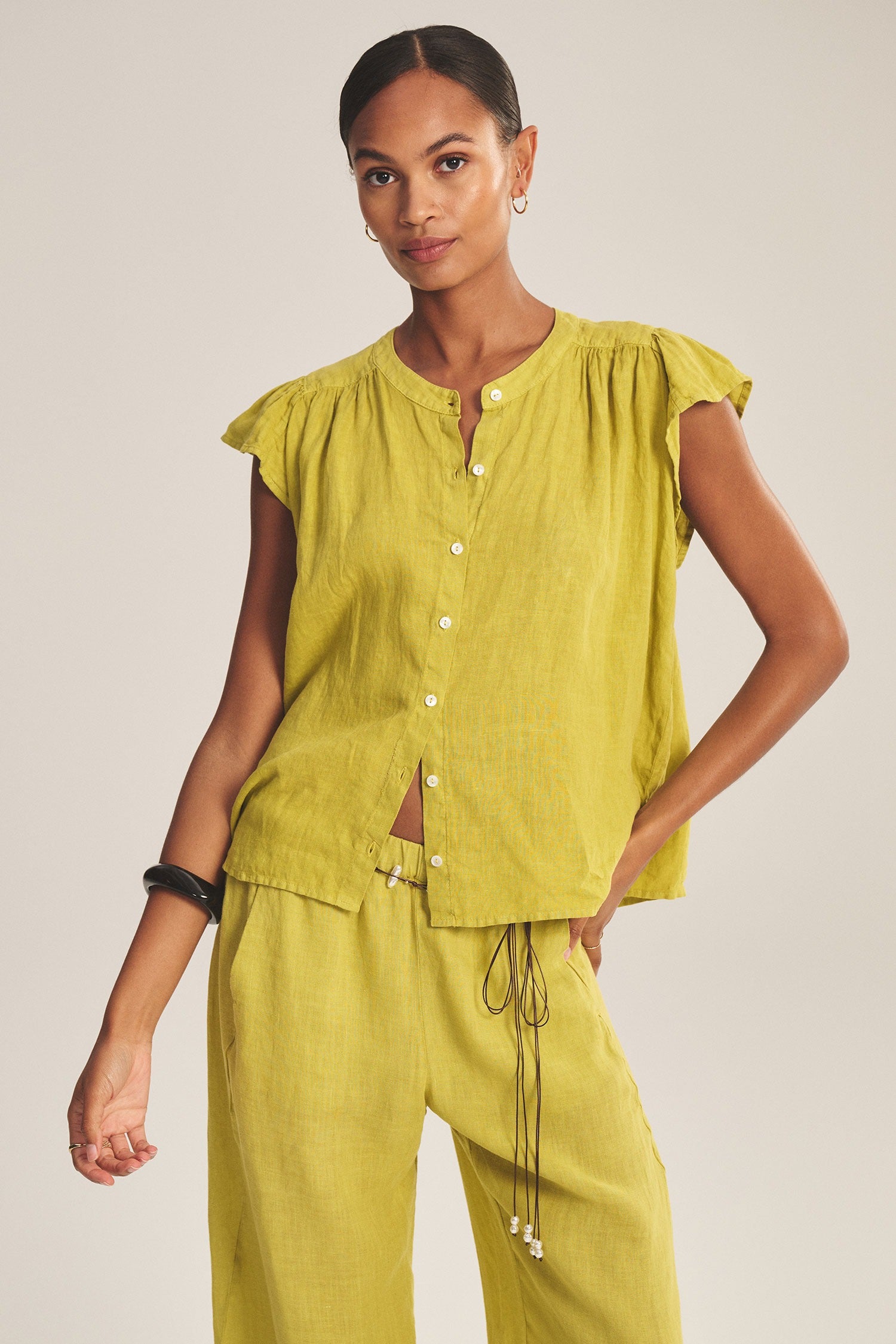 Woman wearing a yellow outfit with ruffled sleeves on a plain background