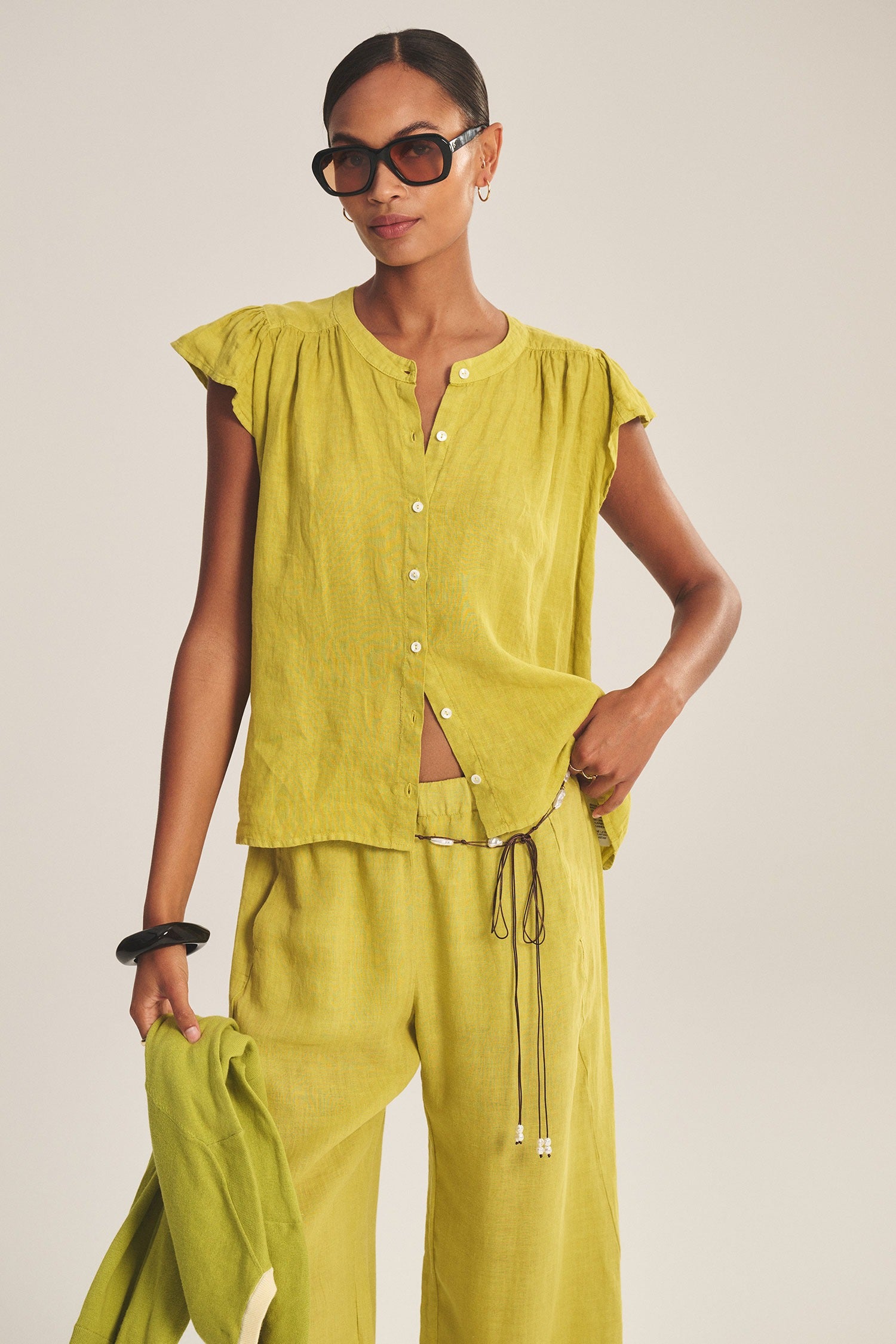 Woman wearing a green outfit with sunglasses on a plain background