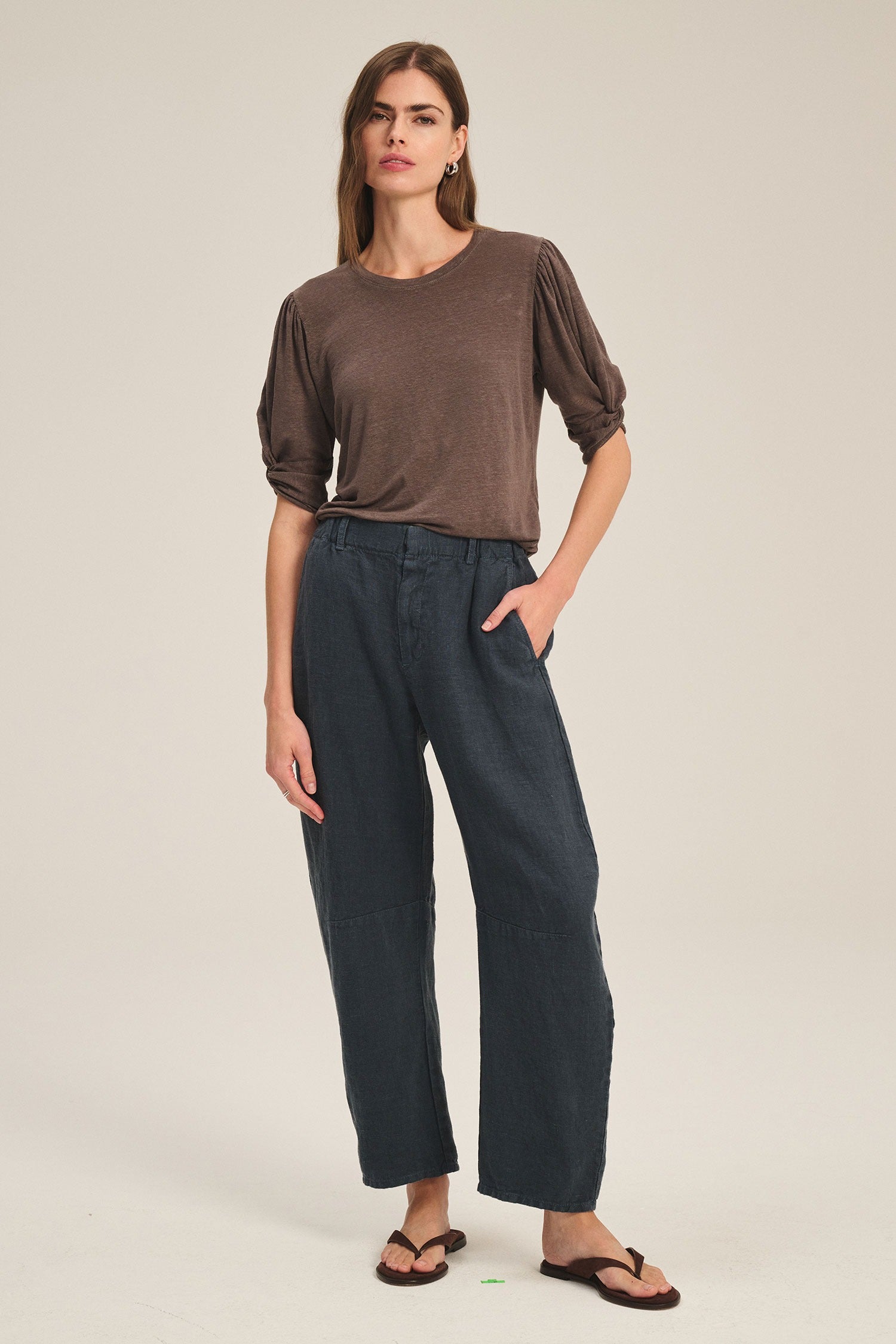 Woman wearing a brown top and dark pants on a beige background