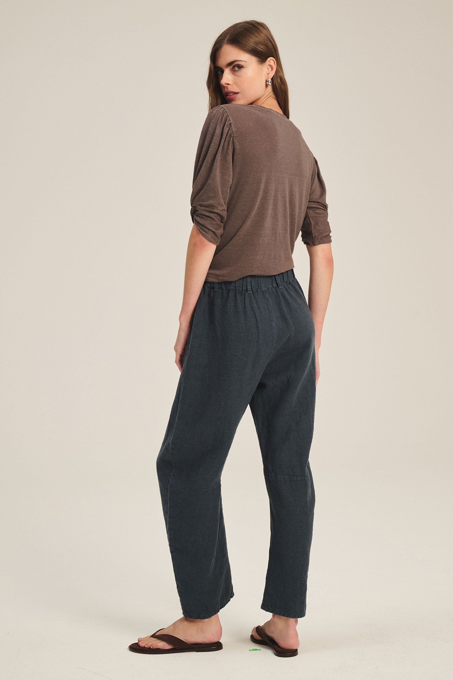 Woman wearing a brown top and dark blue pants on a beige background
