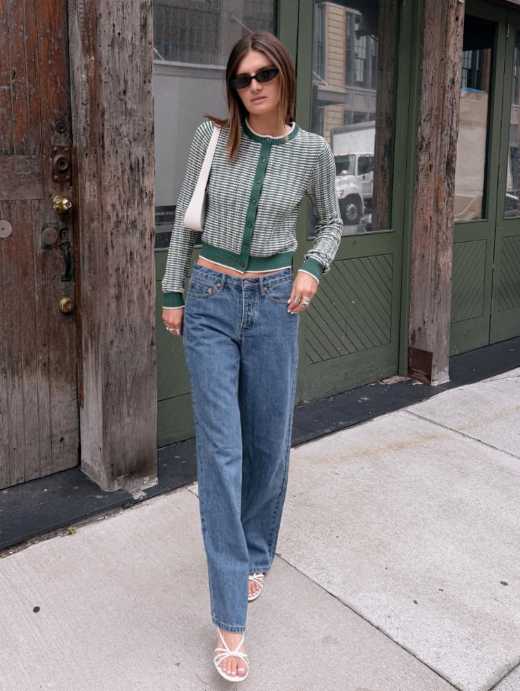 Woman wearing a patterned sweater and blue jeans standing on a sidewalk.