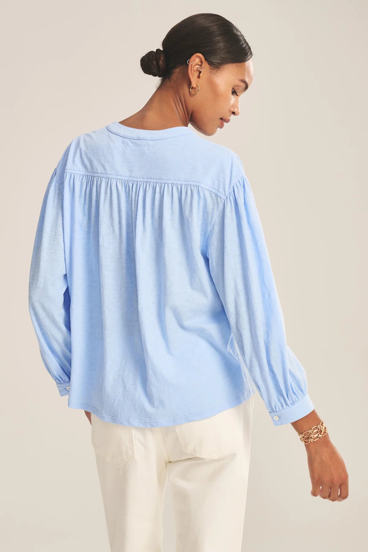 Woman wearing a light blue blouse with long sleeves on a beige background