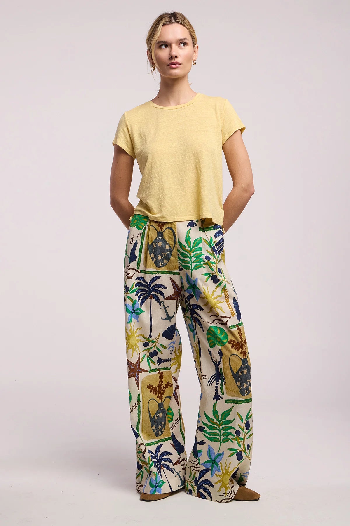Woman wearing a yellow top and colorful patterned pants on a light background