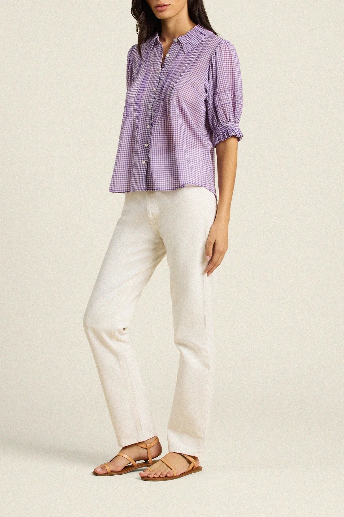 Woman wearing a purple checkered shirt and white pants on a beige background