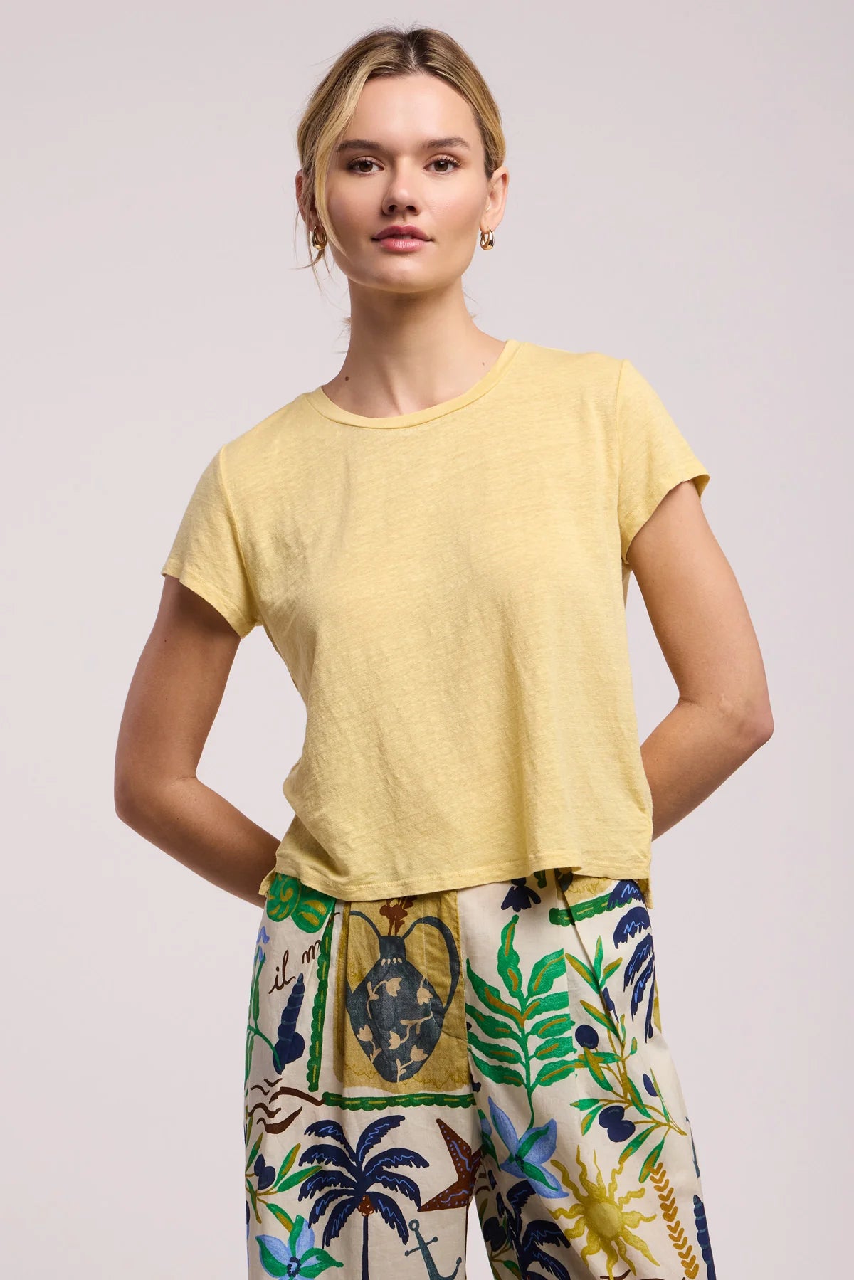 Woman wearing a yellow top and colorful pants on a plain background