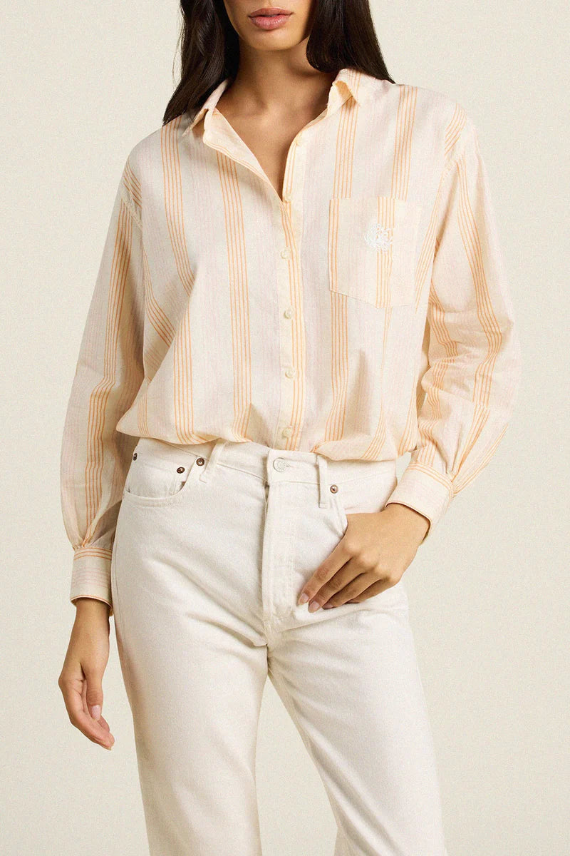 Woman wearing a striped shirt and white pants against a plain background