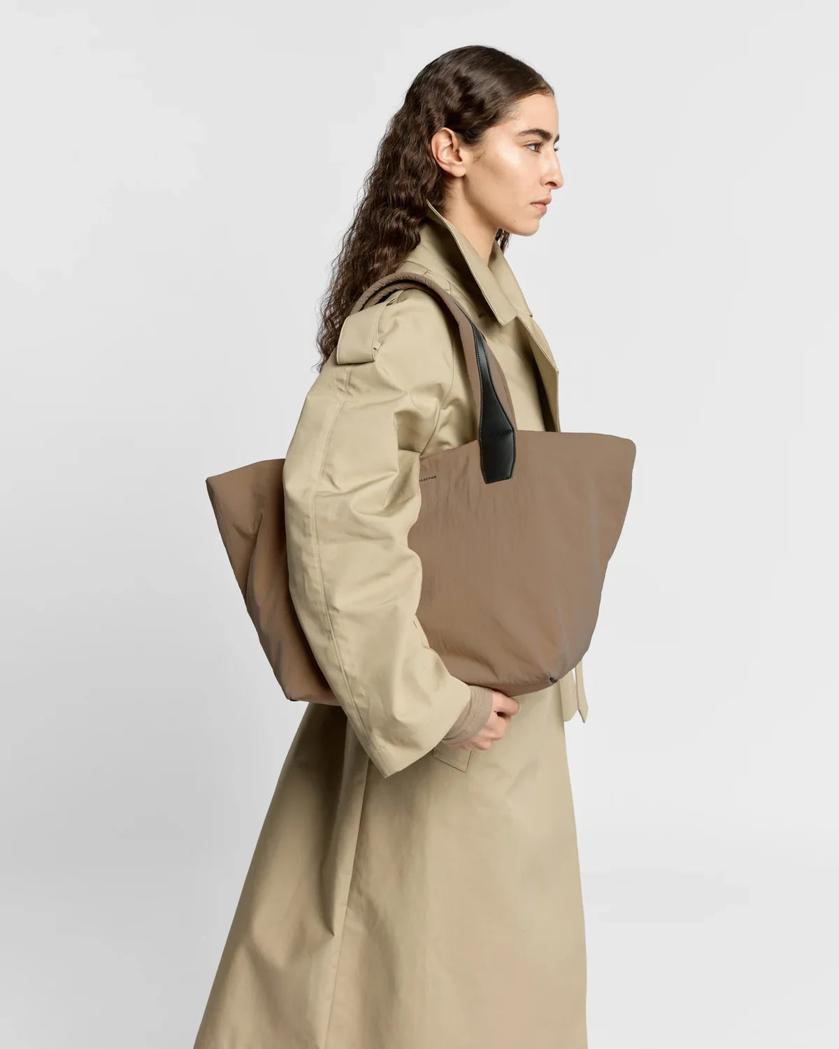 Woman holding a large beige tote bag against a white background