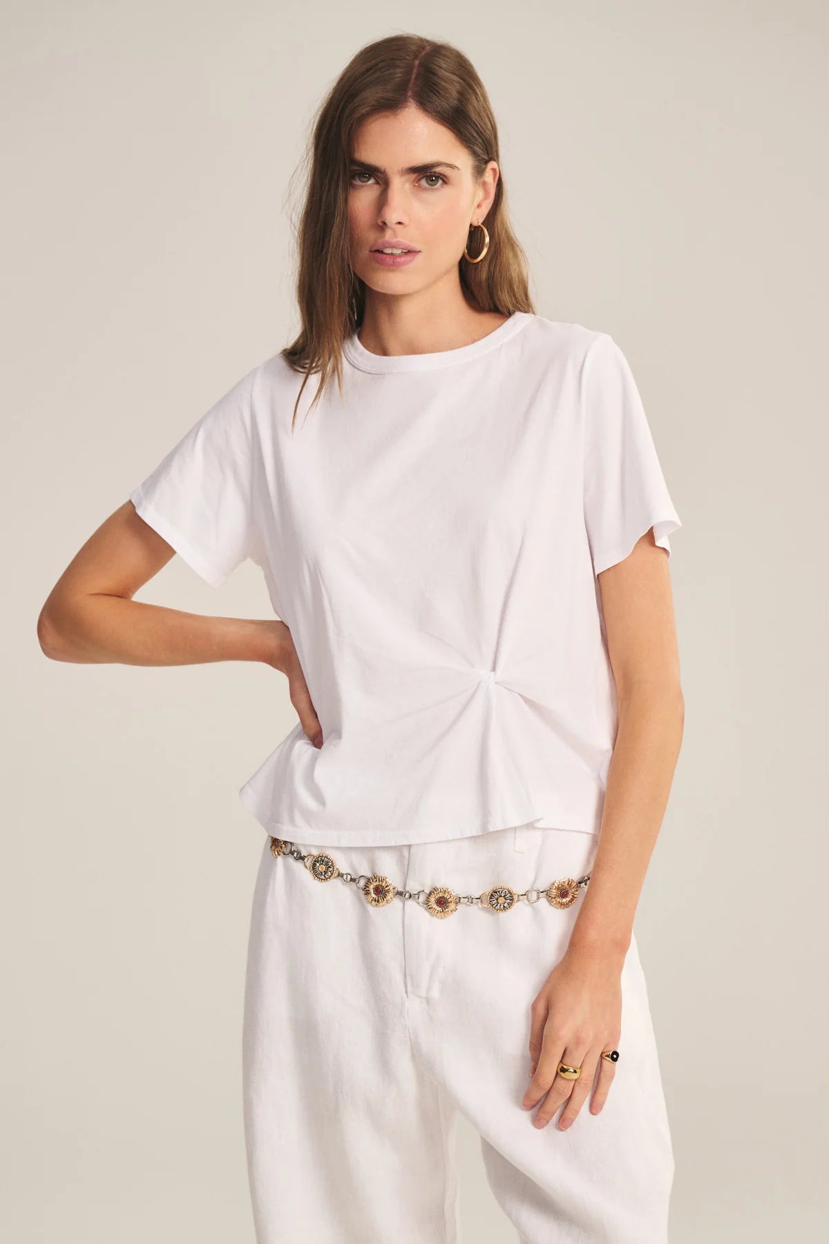 Woman wearing a white outfit with a gold belt on a plain background