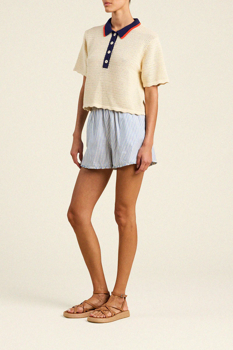 Person wearing a cream-colored polo shirt with red trim and light blue striped shorts on a beige background