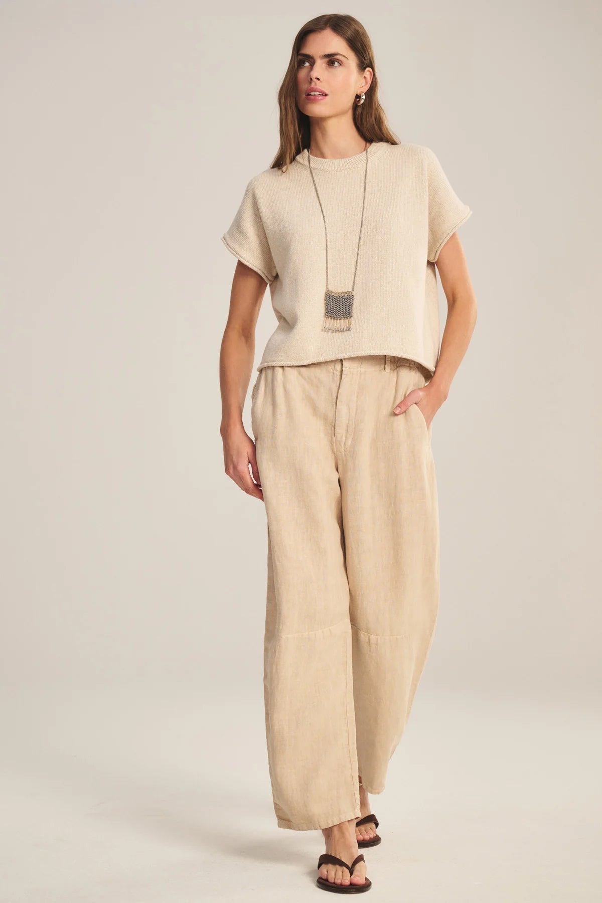 Woman wearing a beige top and wide-leg pants on a plain background