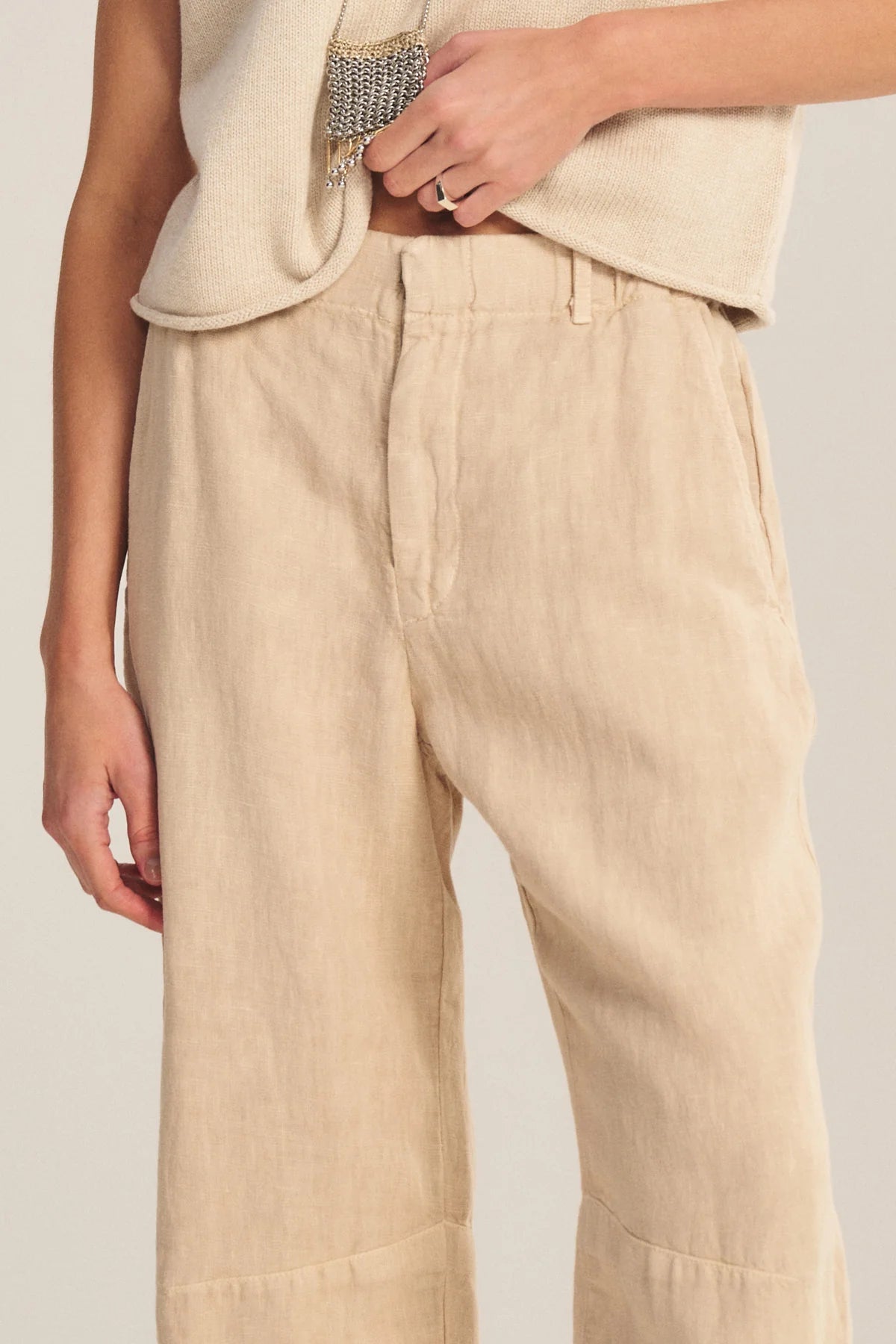 Person wearing beige pants and a cream top on a plain background