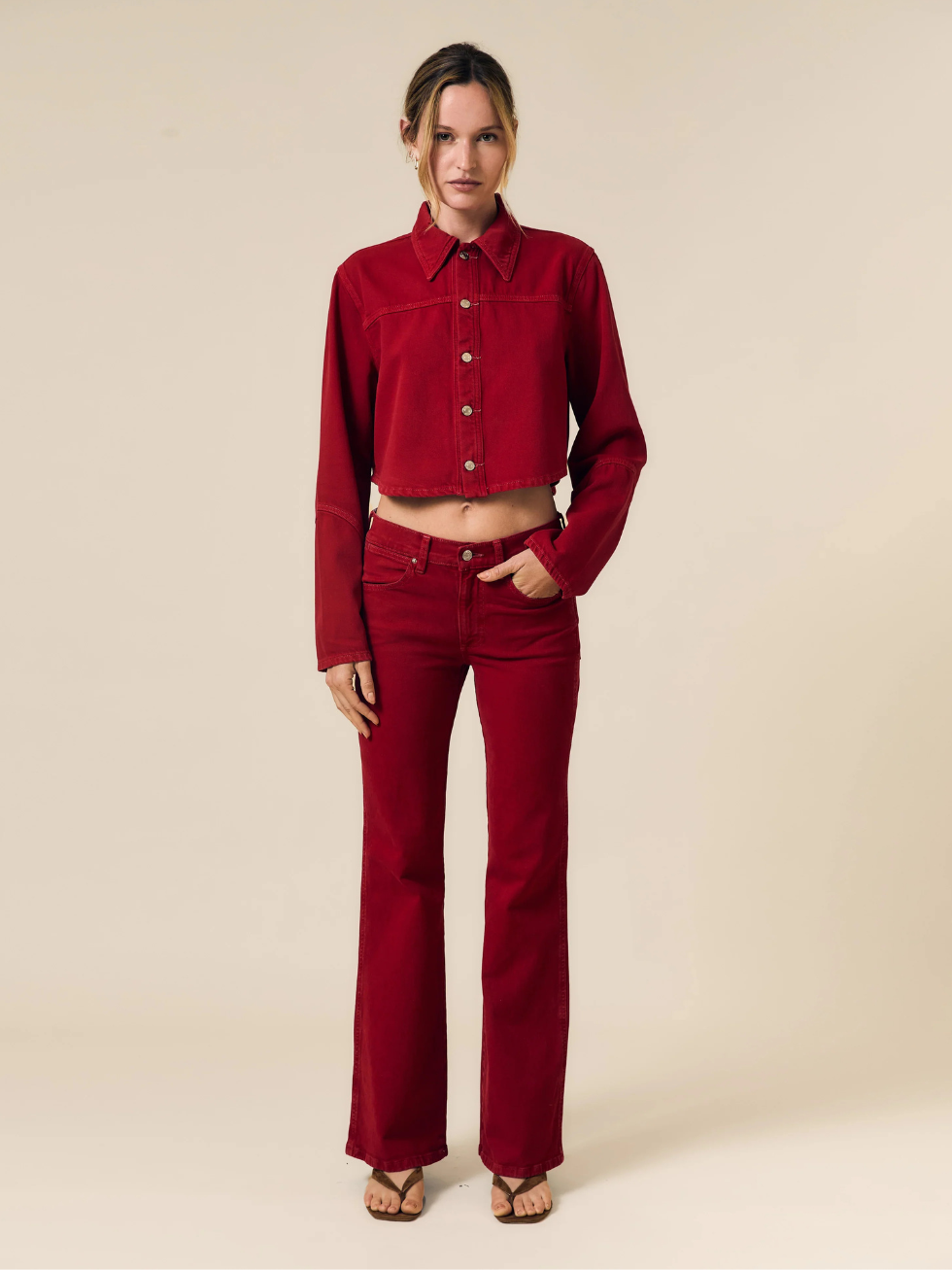 Woman wearing a red denim jacket and pants on a beige background
