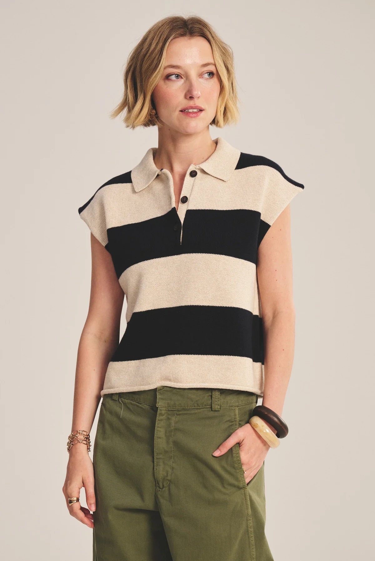 Woman wearing a sleeveless striped shirt and green pants against a plain background