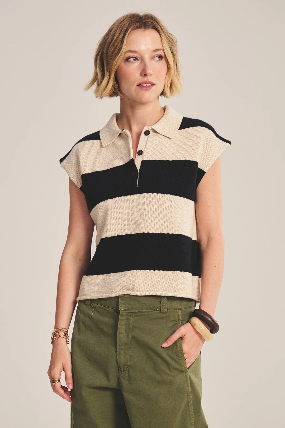 Woman wearing a sleeveless striped shirt and green pants against a plain background