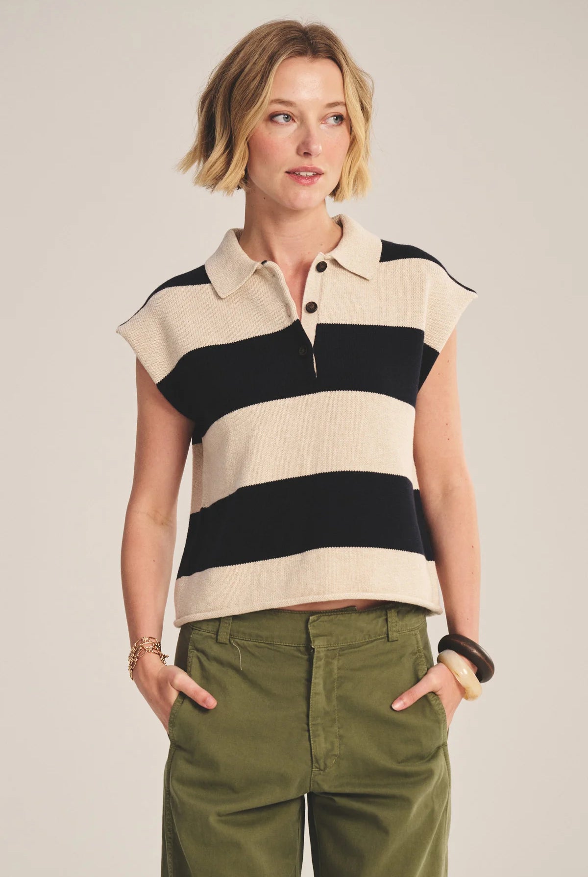 Woman wearing a sleeveless striped shirt and green pants against a plain background