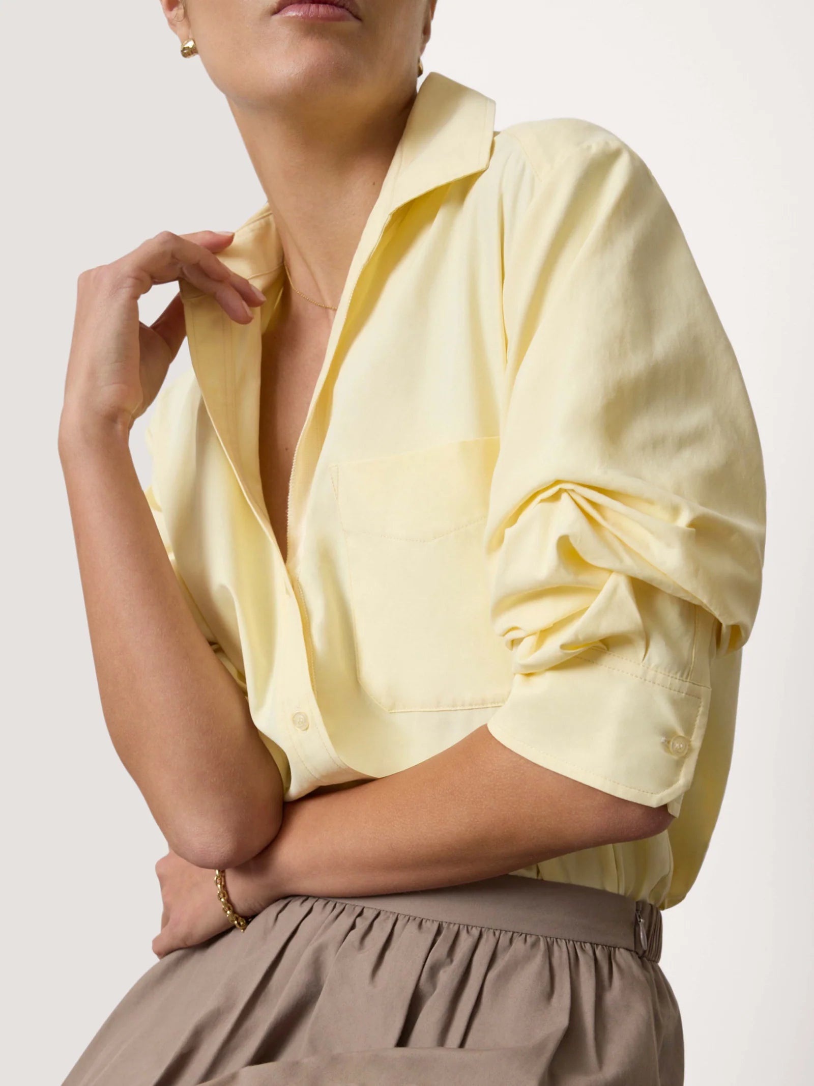 Person wearing a light yellow blouse with rolled-up sleeves on a plain background